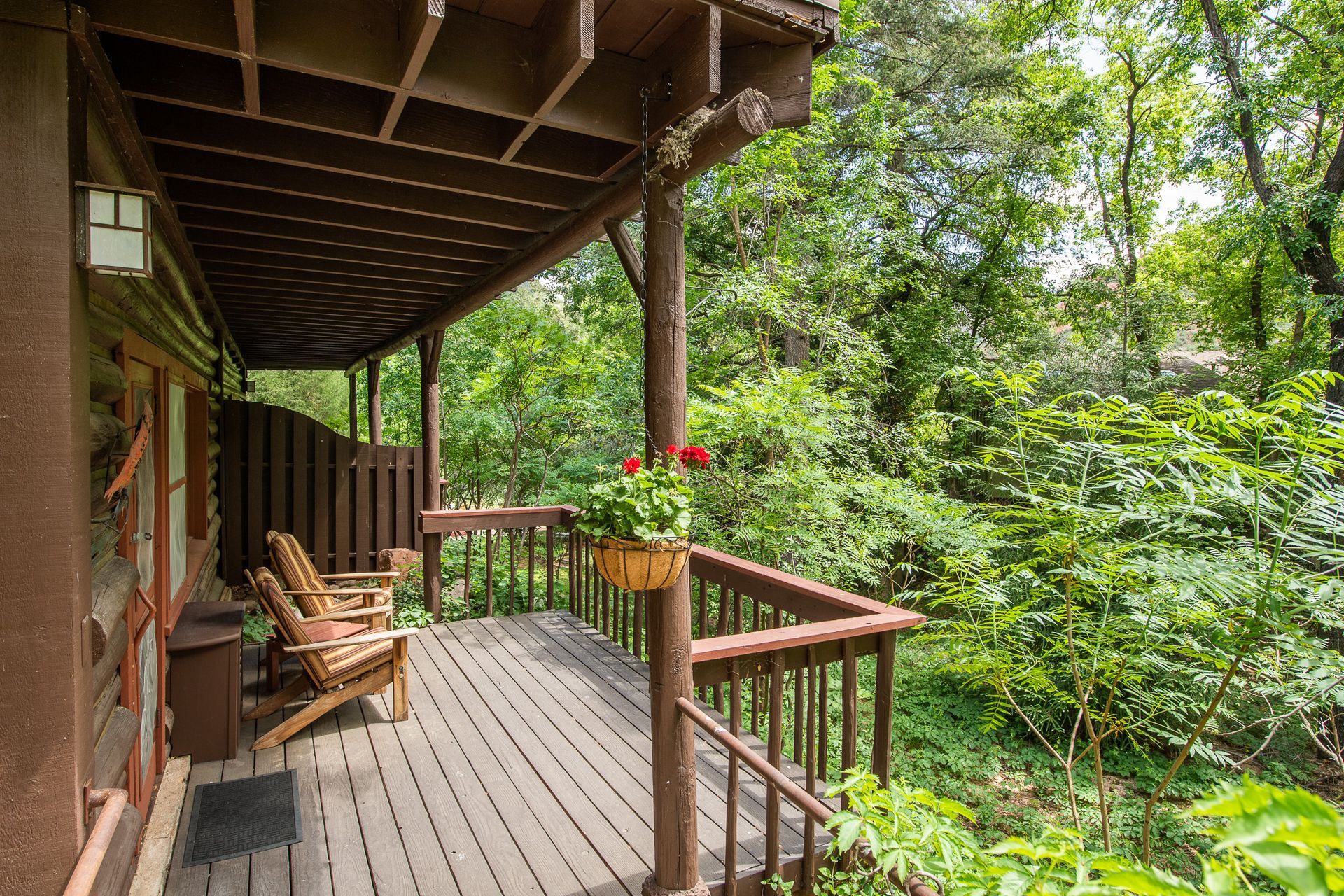 Wooden porch with railing and chairs overlooking lush green forest greenery