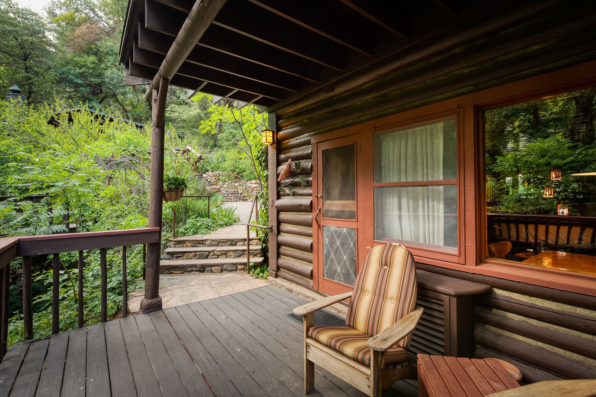 Wooden cabin porch with log walls, cushioned chair, and forest view beyond the railing