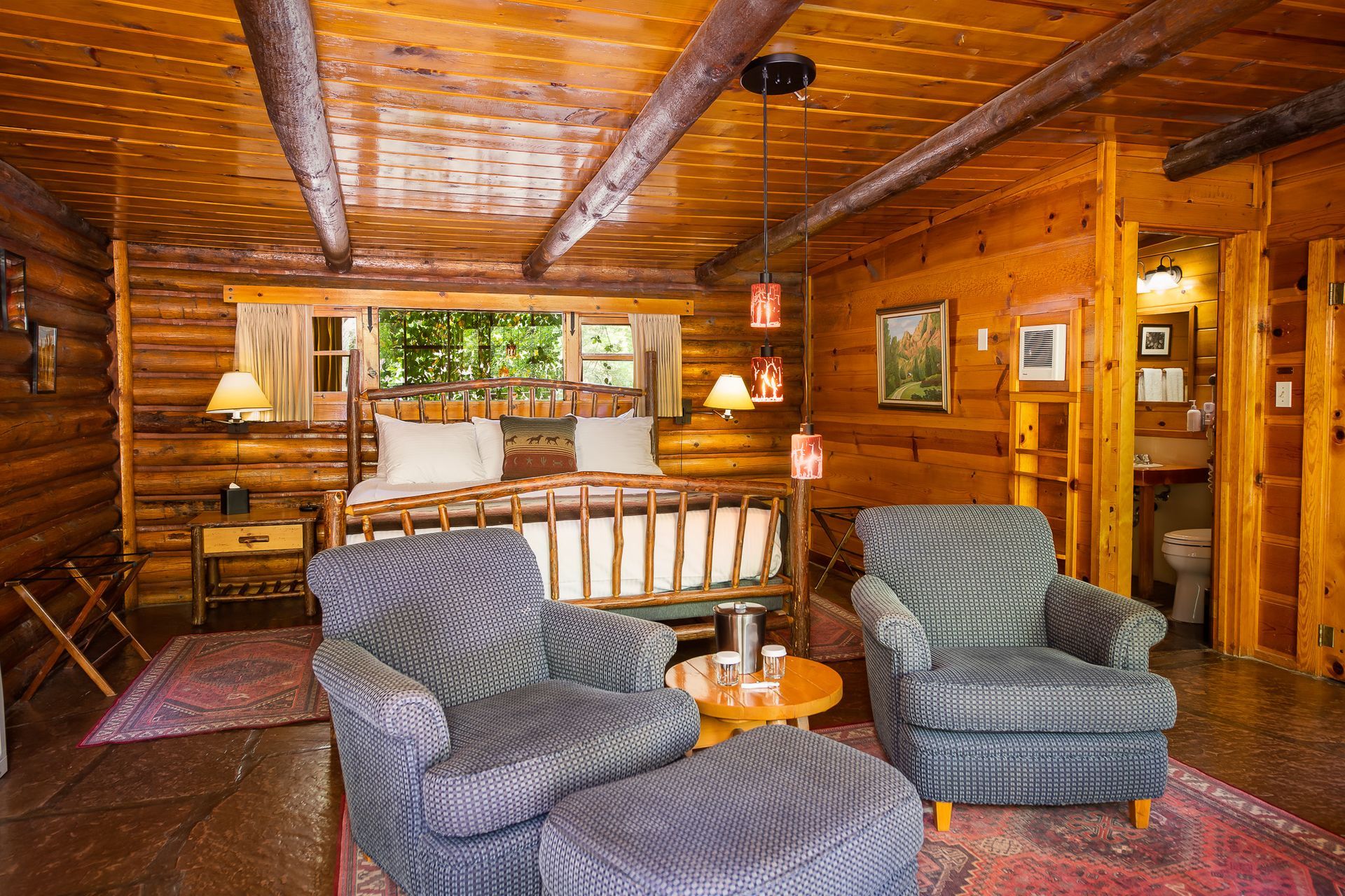 Cozy log cabin living room with patterned chairs, wooden beams, and a striped sofa.