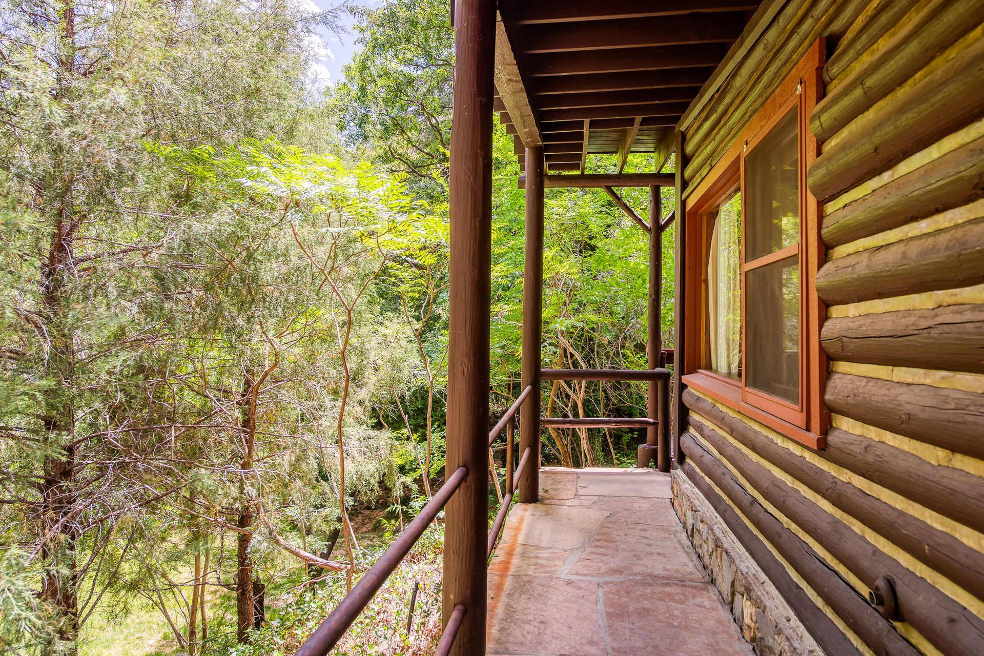 Wooden cabin porch overlooking a green forest, with log siding and railing.