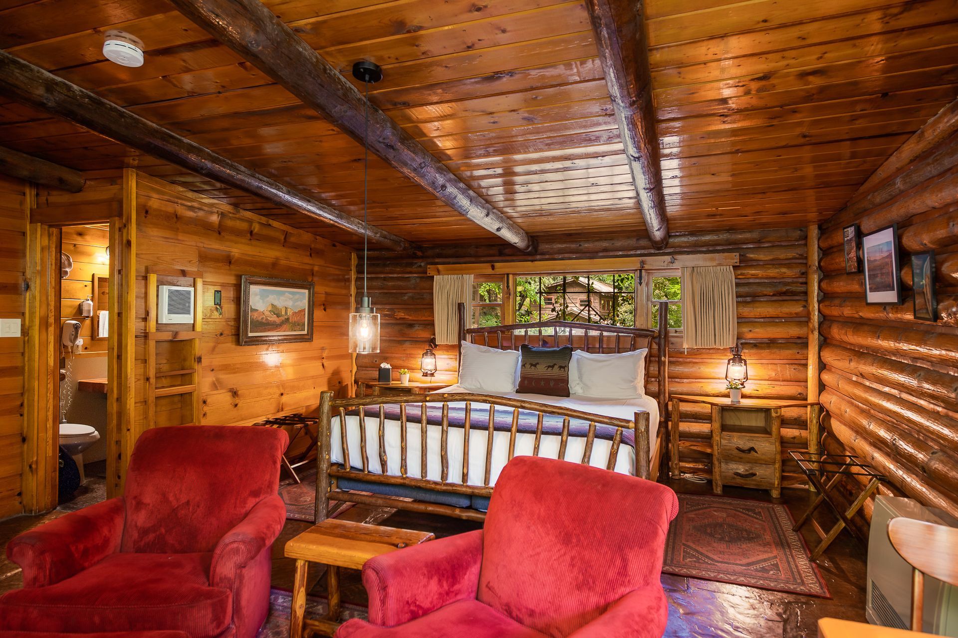 Cozy log cabin bedroom with red chairs, wood-paneled walls, and a bed by a window