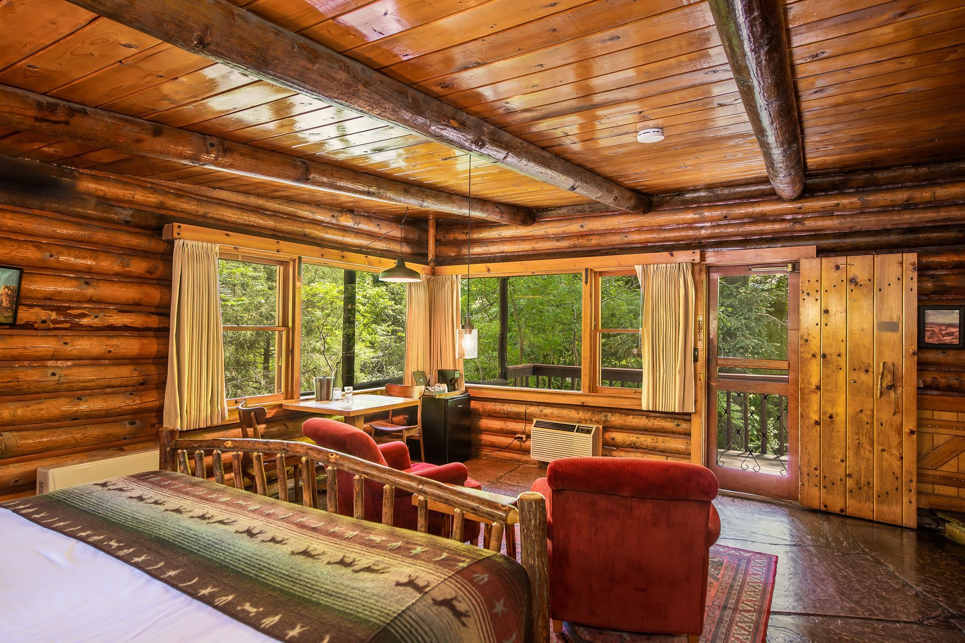 Cozy log cabin living room with red furniture, wood beams, and large windows overlooking greenery