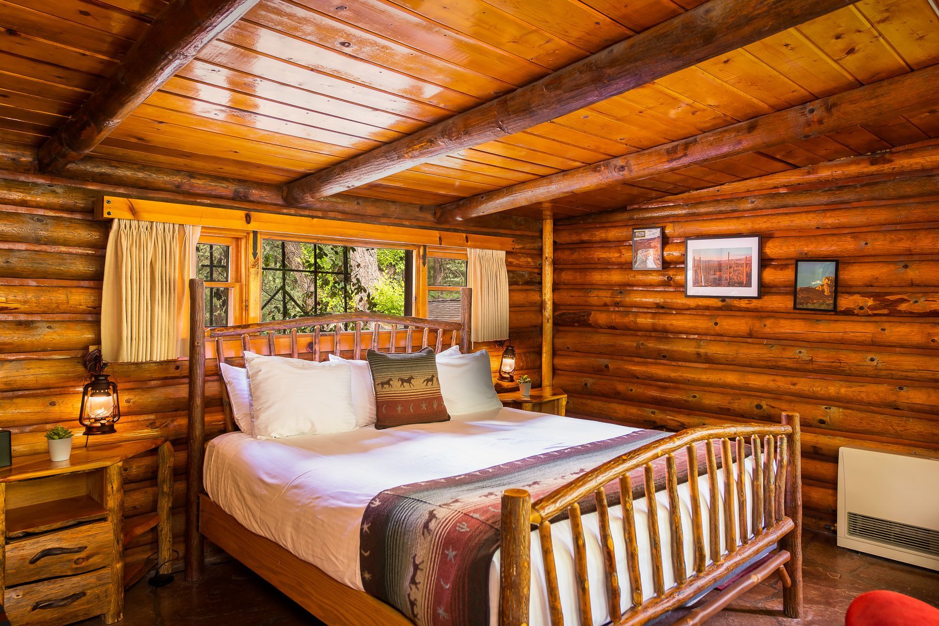 Cozy wooden cabin bedroom with a bed, warm lighting, and a window looking out to greenery