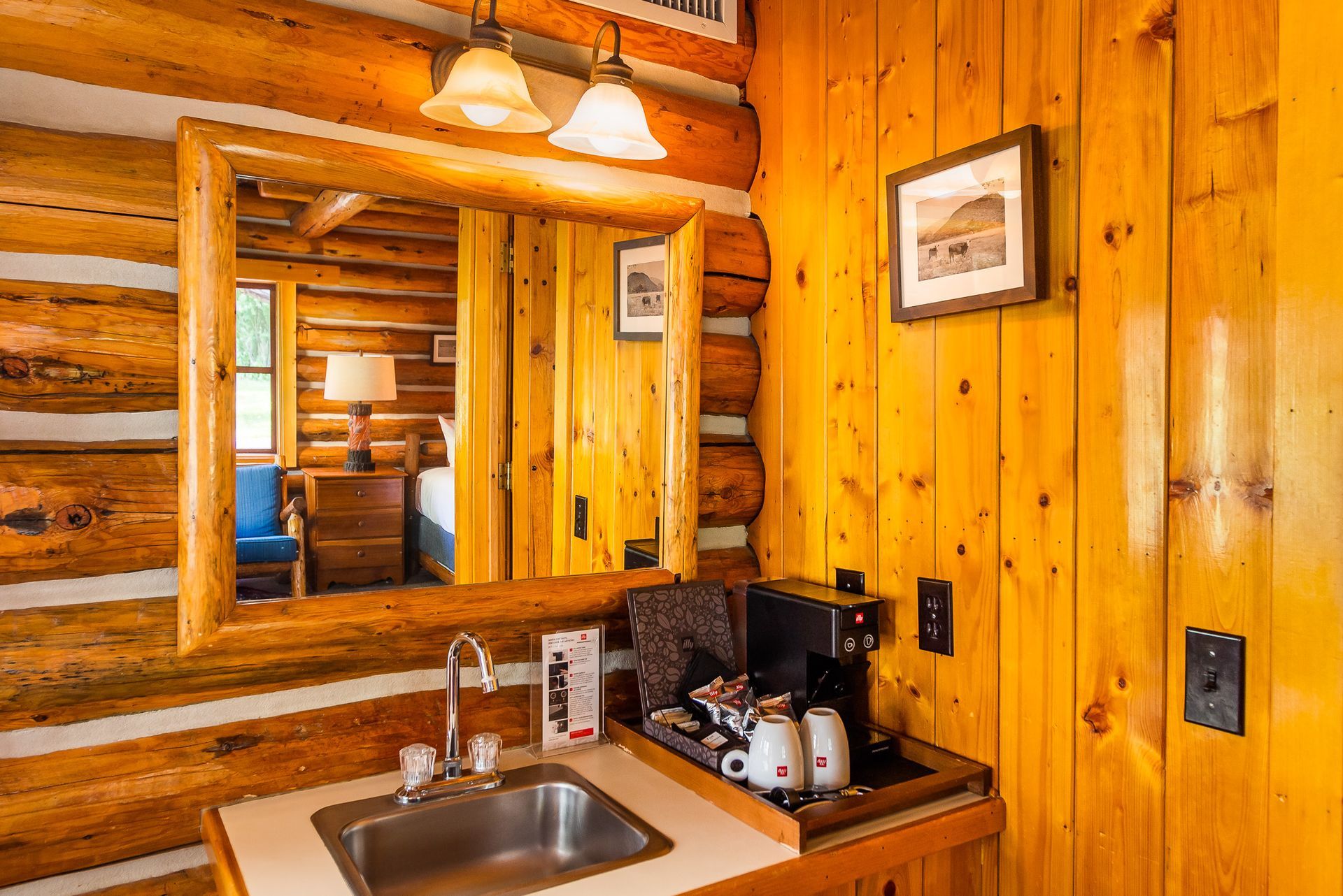 Rustic wooden bathroom vanity with mirror, sink, and coffee maker in a warmly lit cabin interior