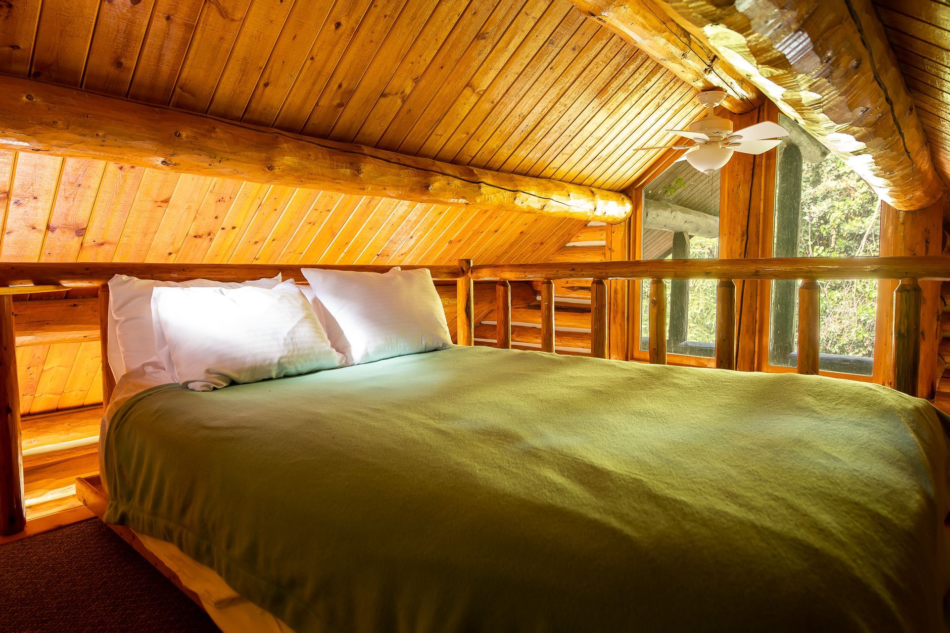 Cozy attic bedroom with a wooden ceiling, log walls, and a bed with white pillows and green bedding