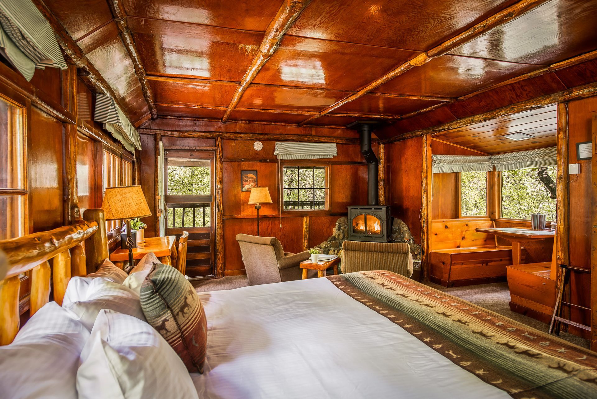 Rustic wooden bedroom with a large bed, windows, and warm amber lighting