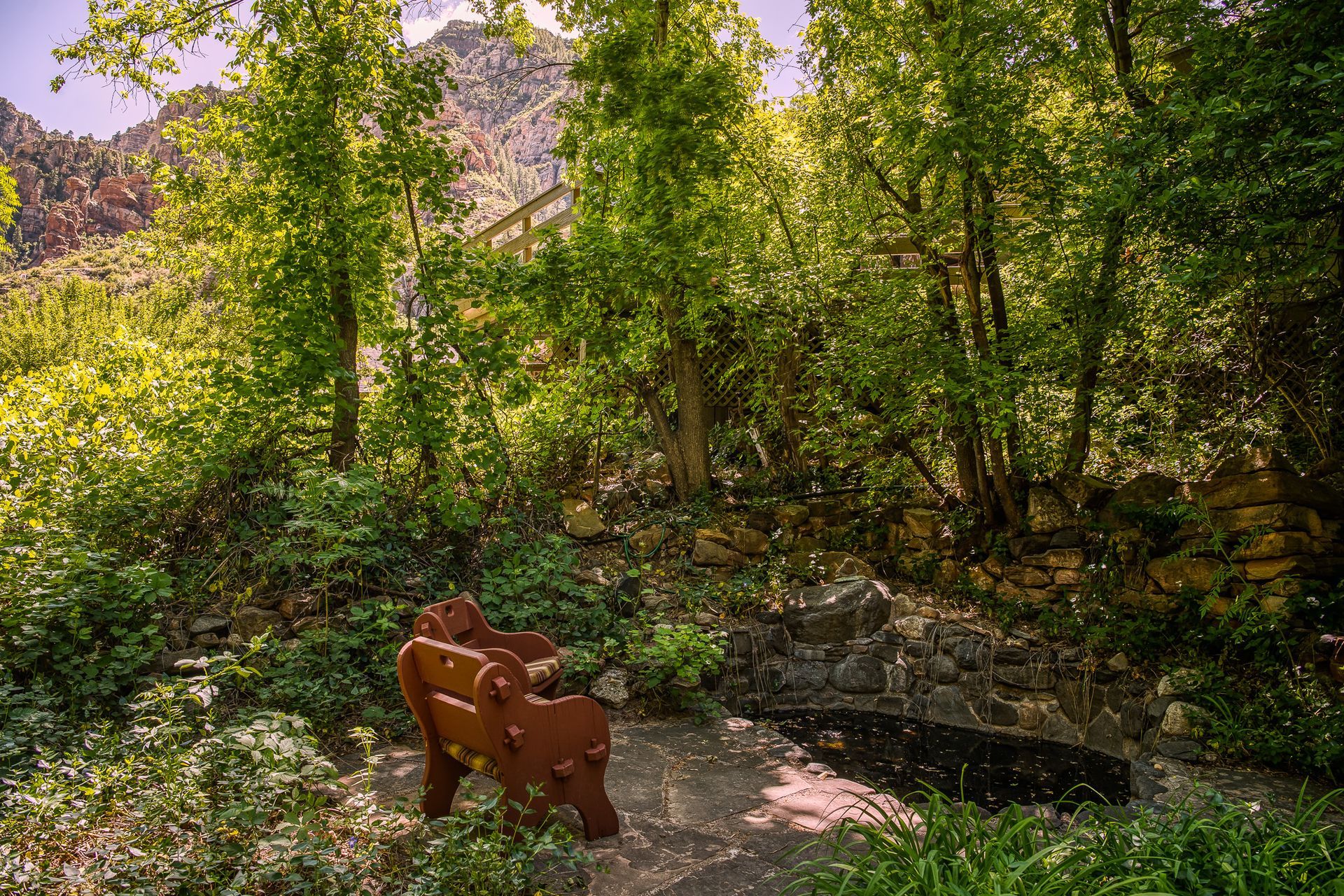 Wooden bench beside a rocky stream in a sunlit green forest