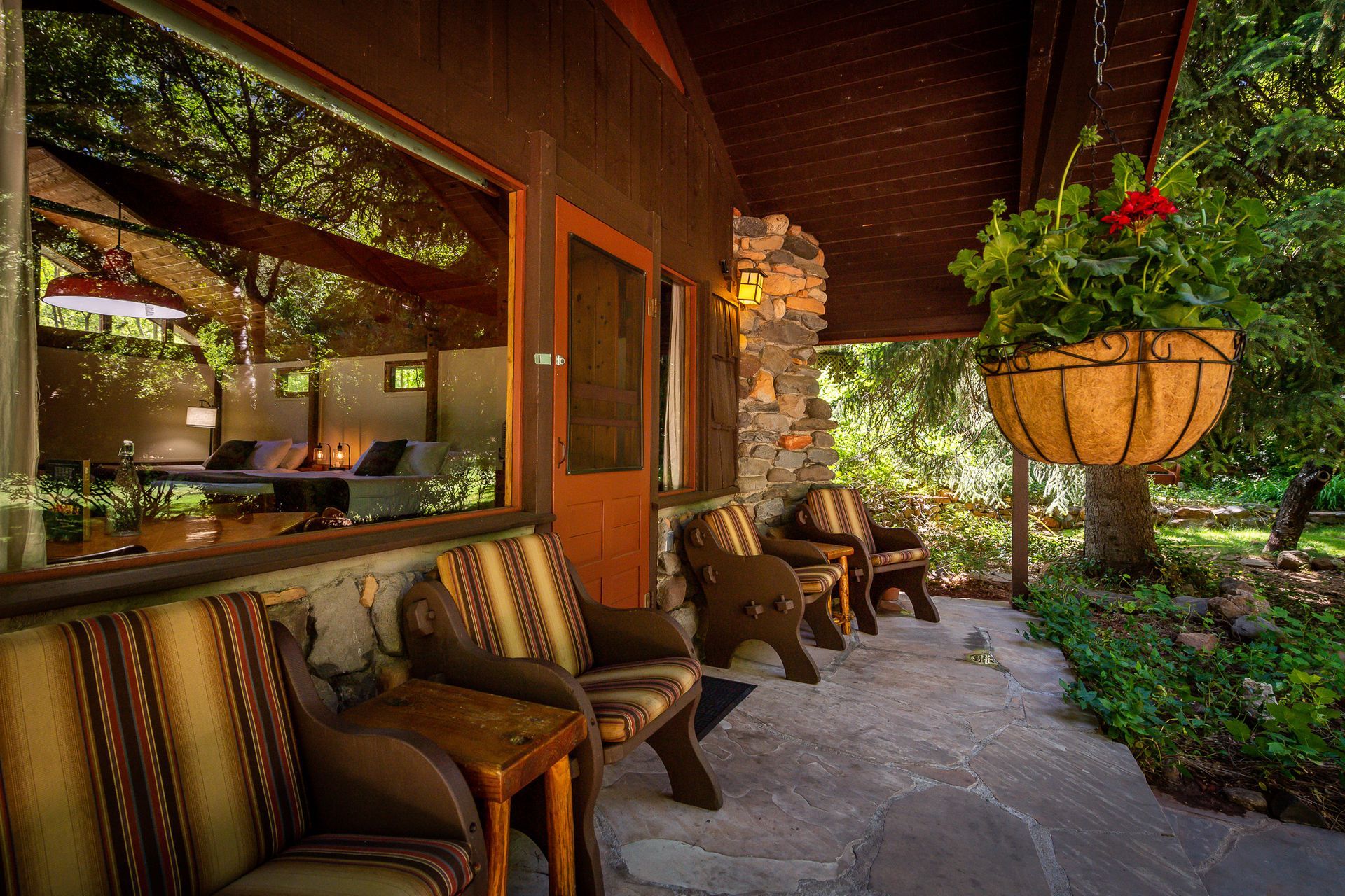 Cozy covered porch with cushioned chairs, wood walls, and hanging plants beside a lush garden path