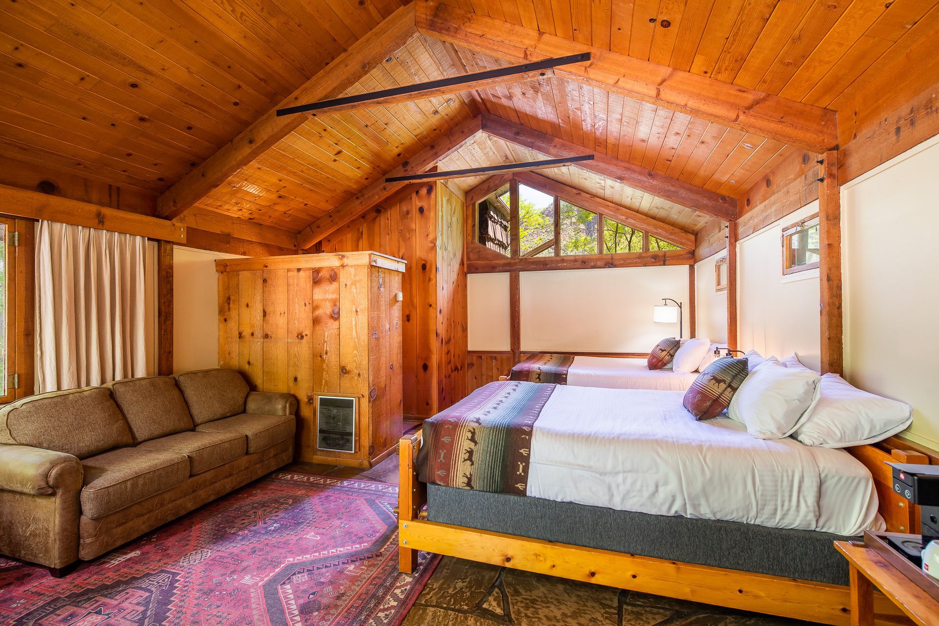 Cozy wood-paneled bedroom with vaulted ceiling, bed, sofa, and patterned rug