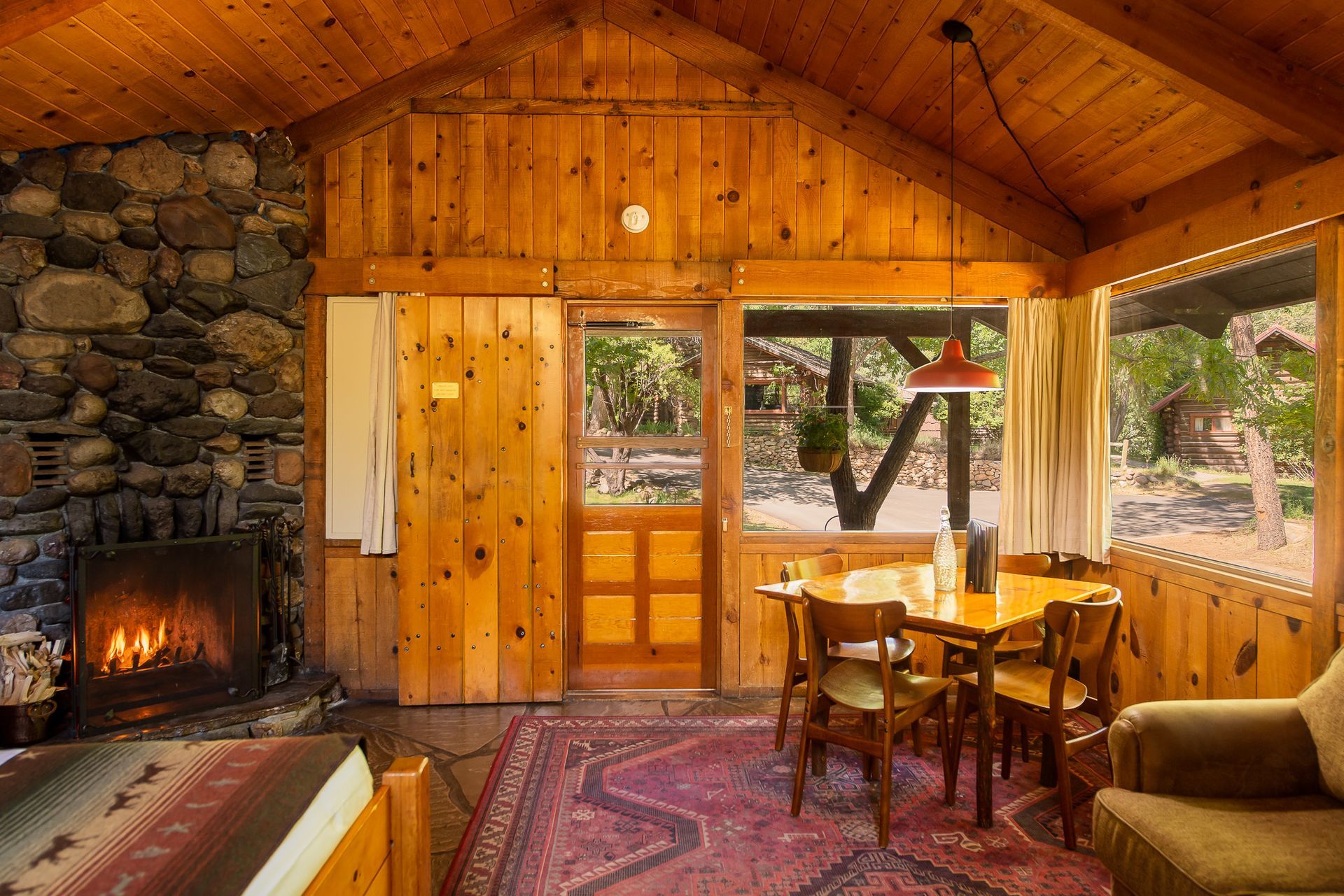 Cozy log cabin living room with stone fireplace, wooden walls, and dining table by large windows