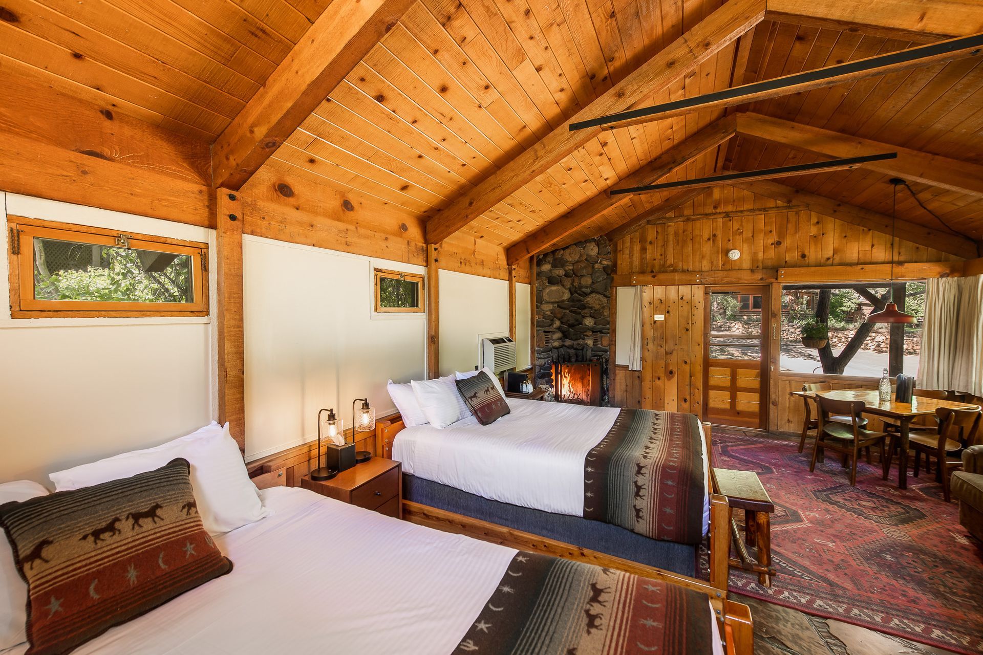Cozy wood-paneled cabin bedroom with two beds, stone fireplace, and sliding doors to a deck
