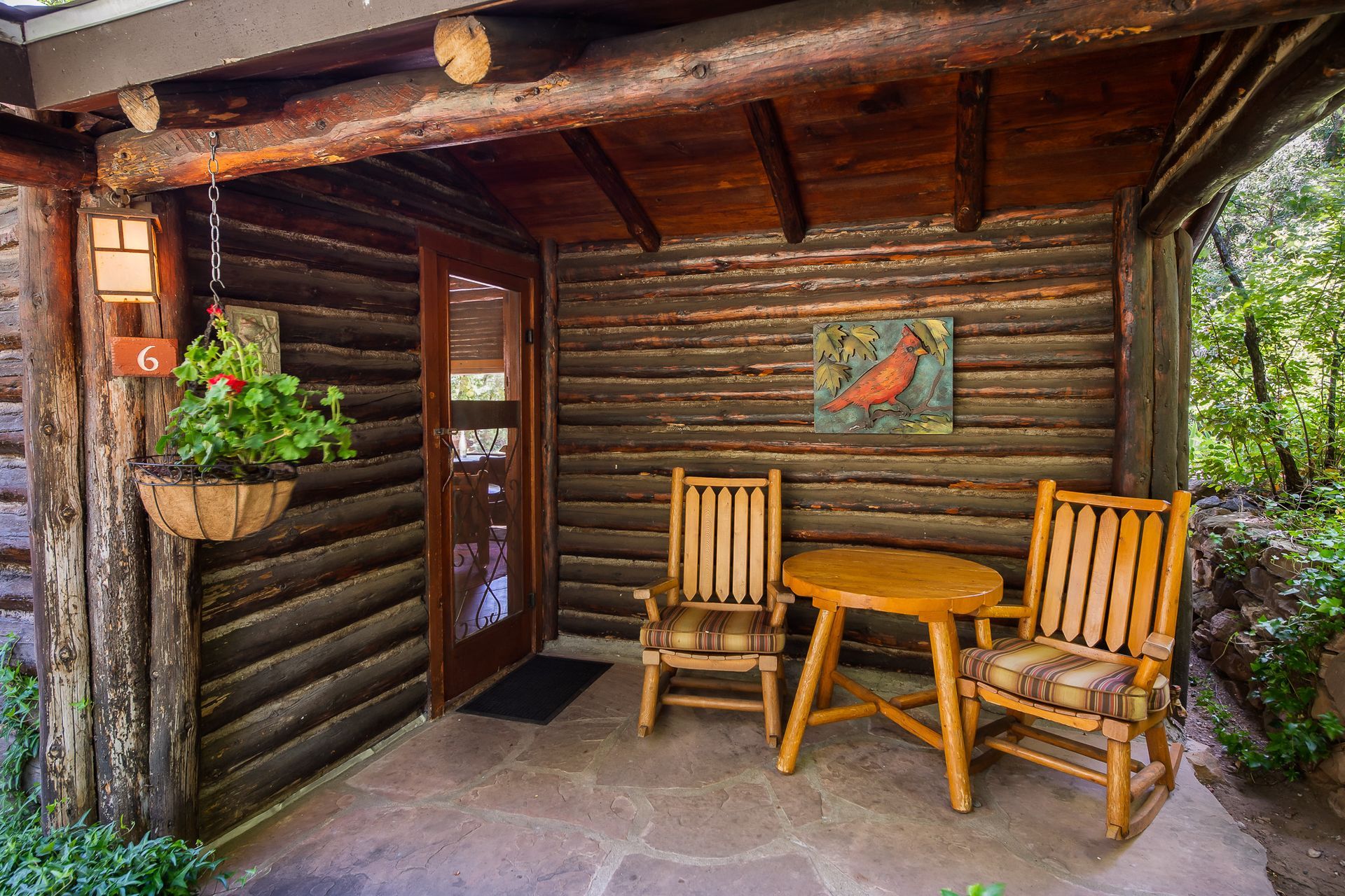 Rustic porch with wooden bench, table, log walls, and a potted plant by the door