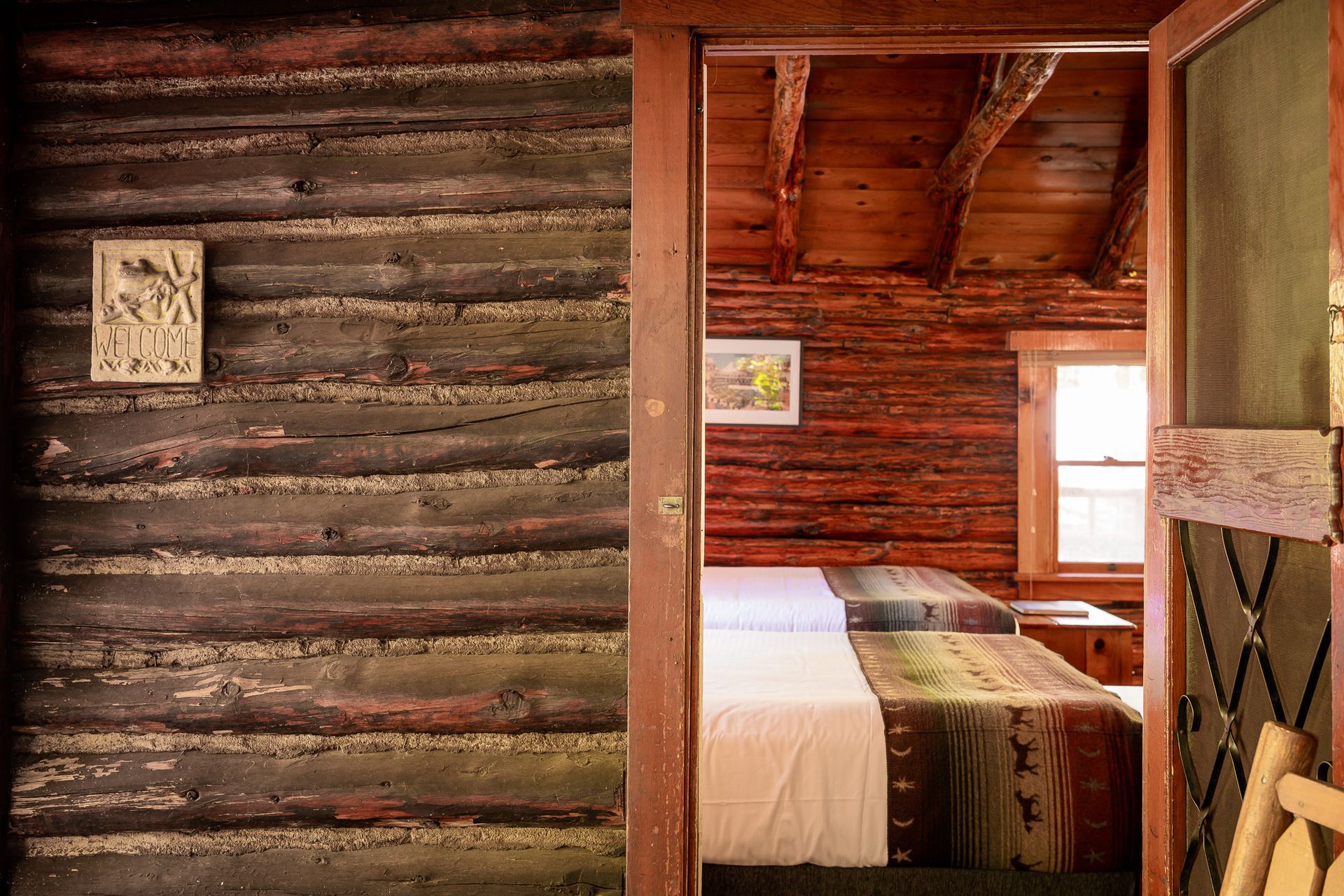 Rustic cabin bedroom seen through a doorway, with log walls, a bed, and warm wood interior.