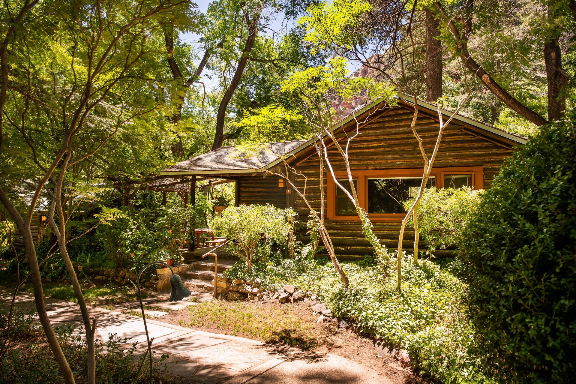 Wooden cabin nestled in lush green forest with a sunlit path in front
