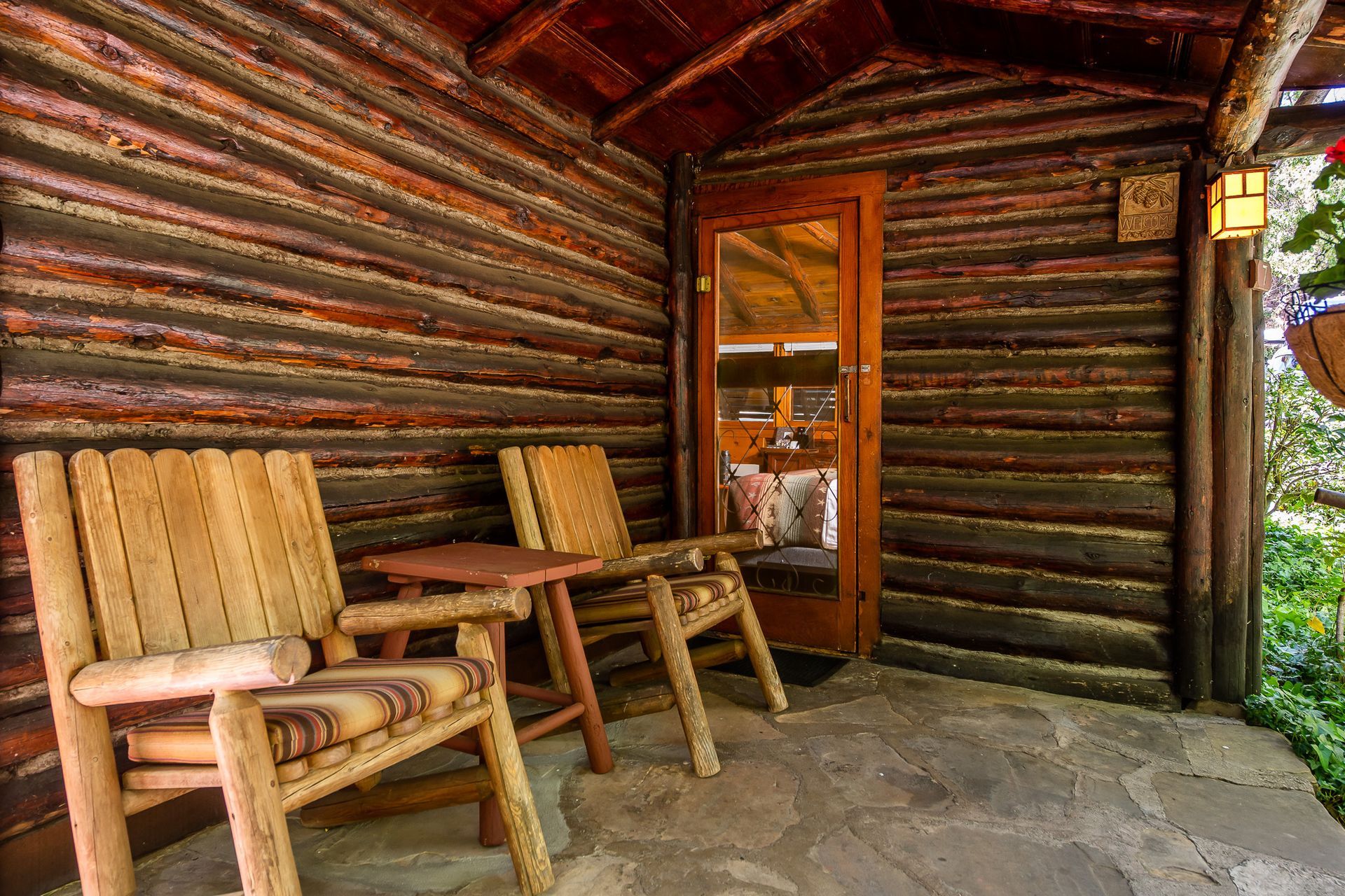 Rustic porch with wooden chairs, small table, and log walls around a cabin entrance