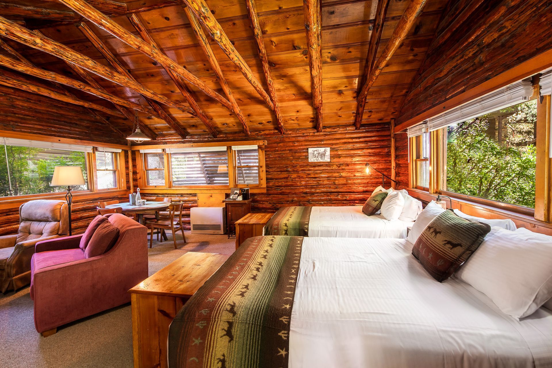 Rustic cabin bedroom with wooden walls, a large bed, and cozy lounge chairs by big windows