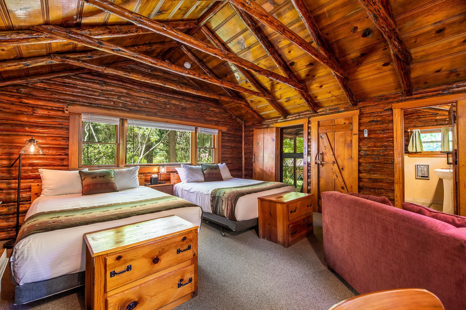 Rustic wooden bedroom with two beds, large window, and cozy seating area