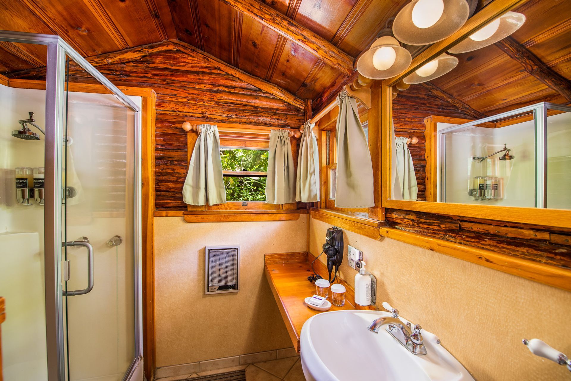 Rustic bathroom with wood-paneled ceiling, shower stall, sink, and large mirror.