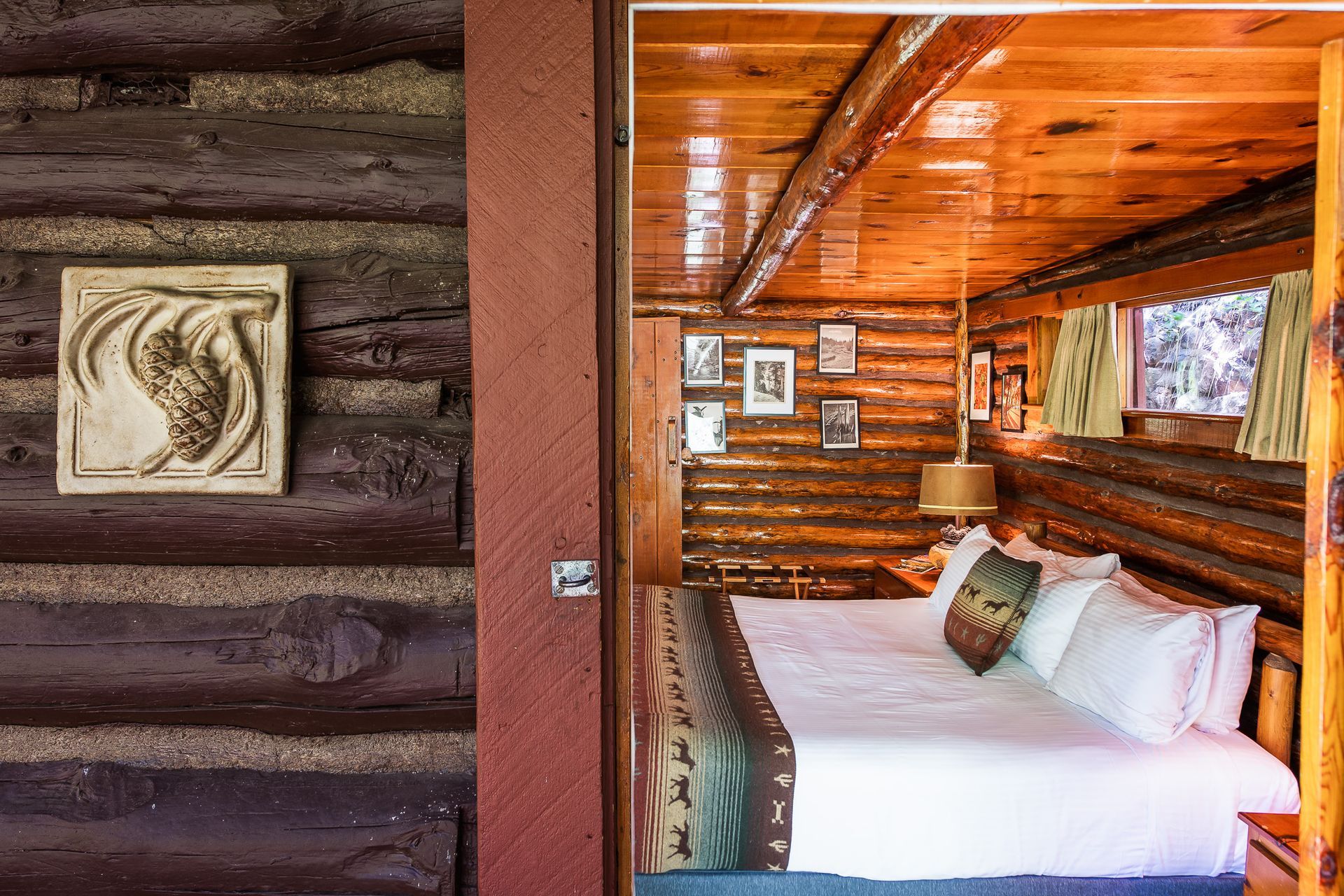 Rustic log cabin bedroom with a bed, pillows, wooden walls, and framed artwork by a window