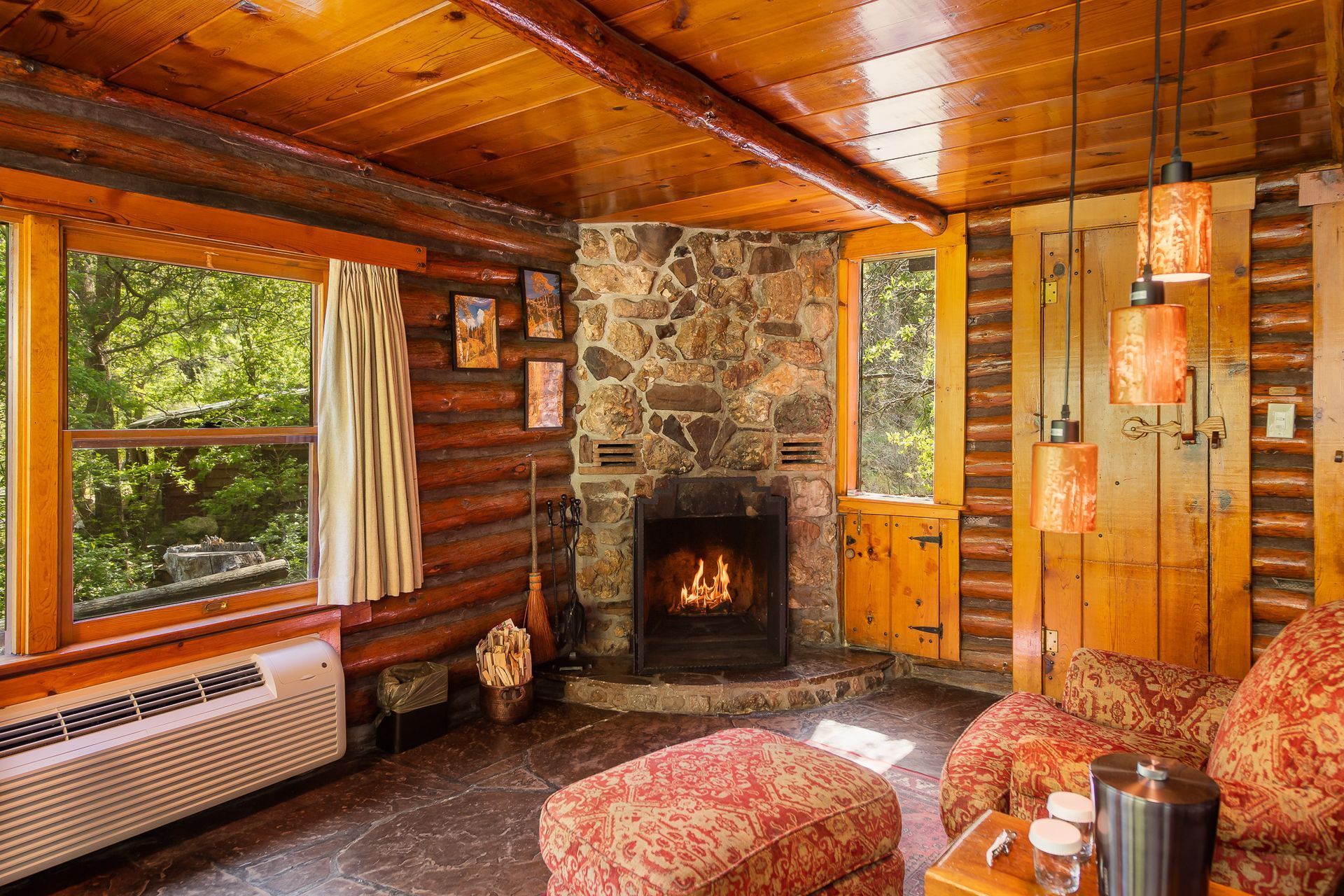Cozy log cabin living room with stone fireplace, wooden walls, large window, and plaid furniture