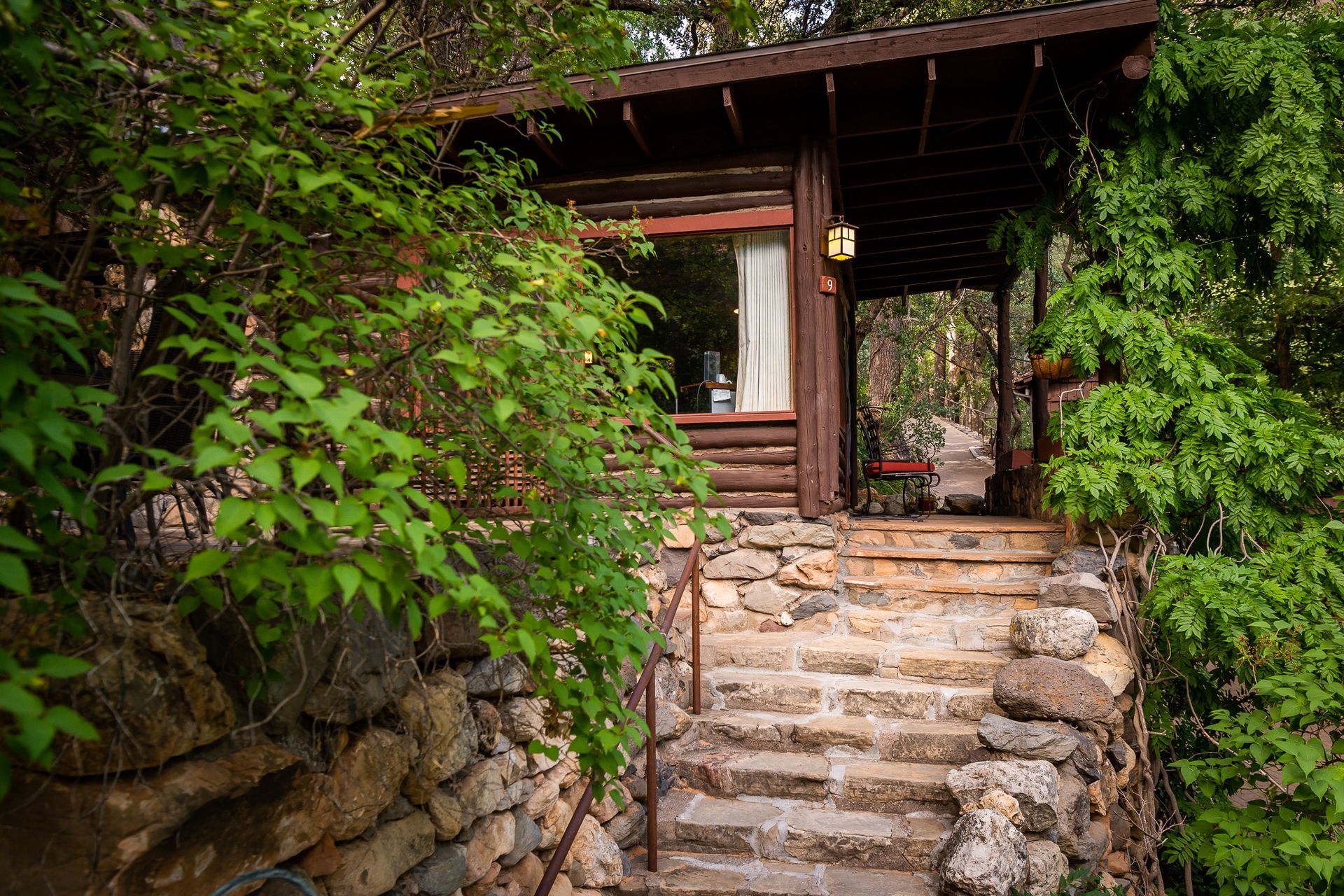 Rustic stone steps leading to a wooden cabin entrance surrounded by dense green foliage.