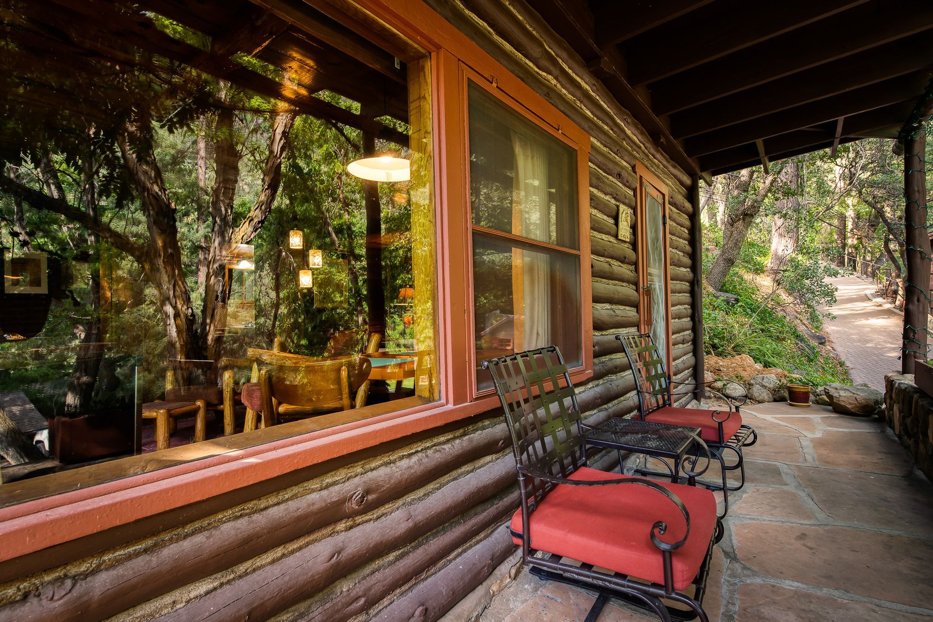 Log cabin porch with red benches, large window reflections, and forest path beside it