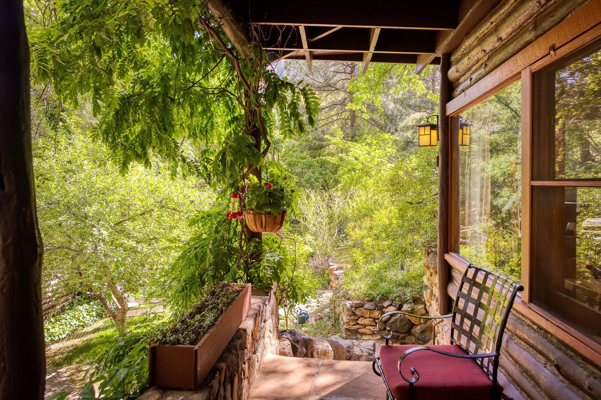 Shaded porch with hanging plants, wooden bench, and lush green garden view