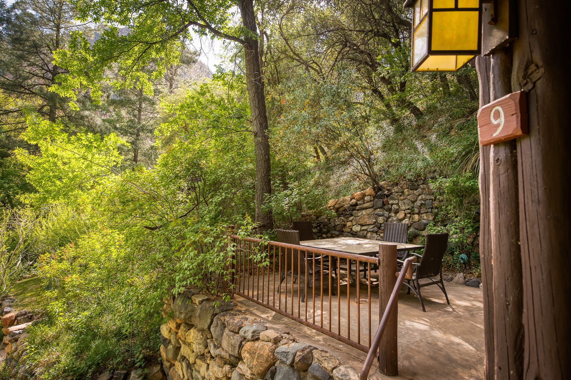 Wooden deck with railing beside a forested walkway in dappled sunlight