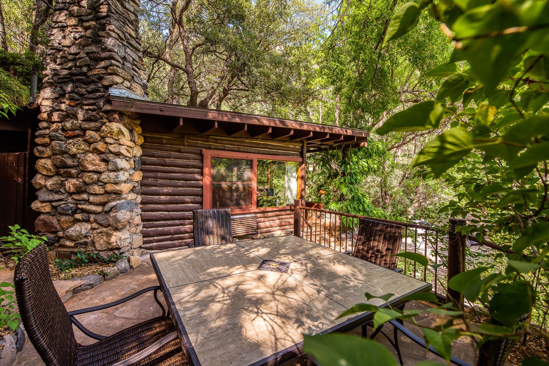 Stone cabin deck with wicker chairs and railing, surrounded by trees and greenery