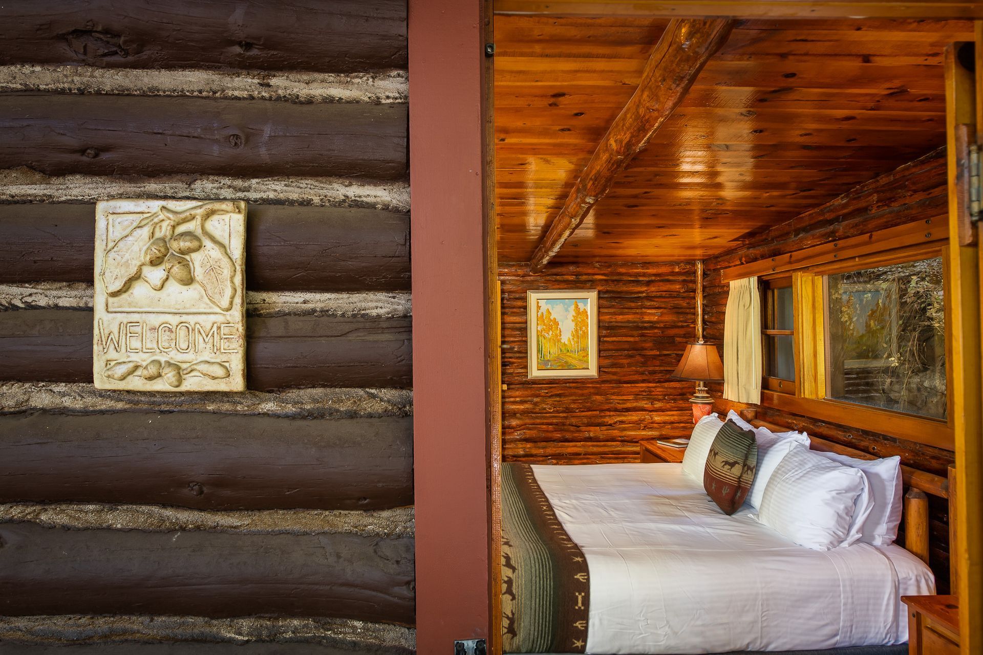 Rustic log cabin bedroom with a neatly made bed, wood-paneled walls, and framed wall art