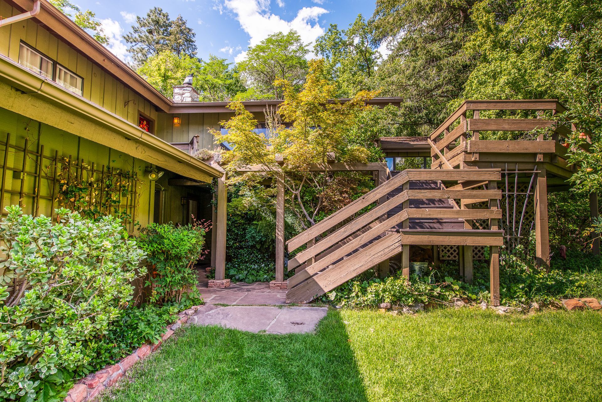 Courtyard garden with green lawn, shrubs, and a wooden staircase beside a building