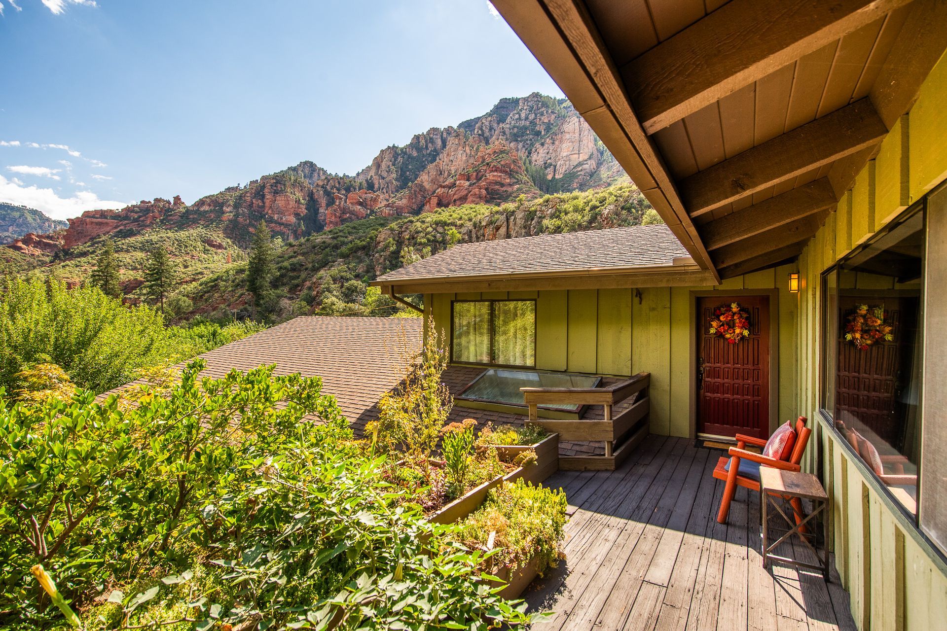 Mountain cabin deck with red chairs, wooden table, and mountain views under a sunlit roof