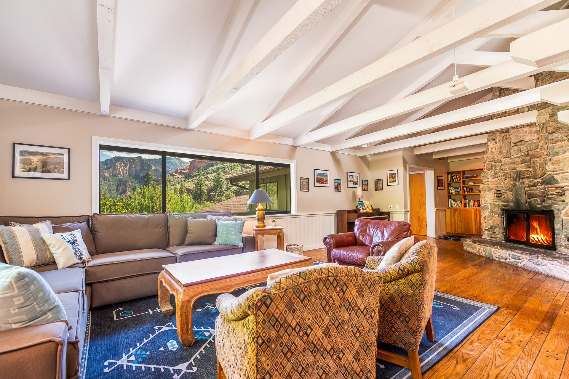 Cozy living room with sectional sofa, coffee table, red chair, stone fireplace, and exposed beam ceiling
