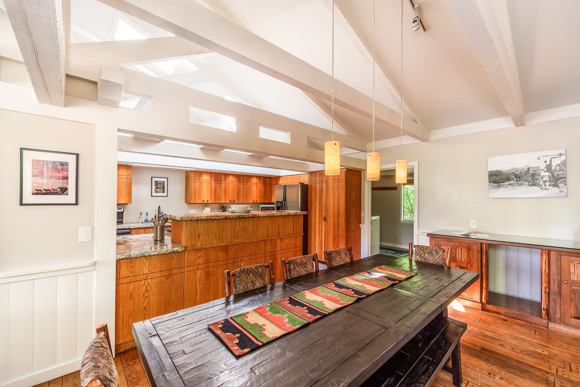 Open-concept kitchen and dining room with wood cabinets, vaulted ceiling, and long dark dining table