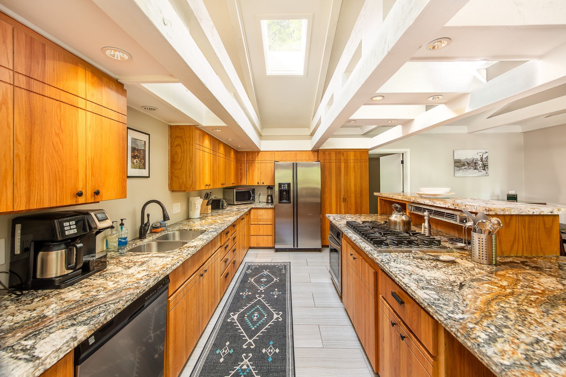 Bright kitchen with wood cabinets, granite counters, stainless fridge, and a long island under recessed lighting