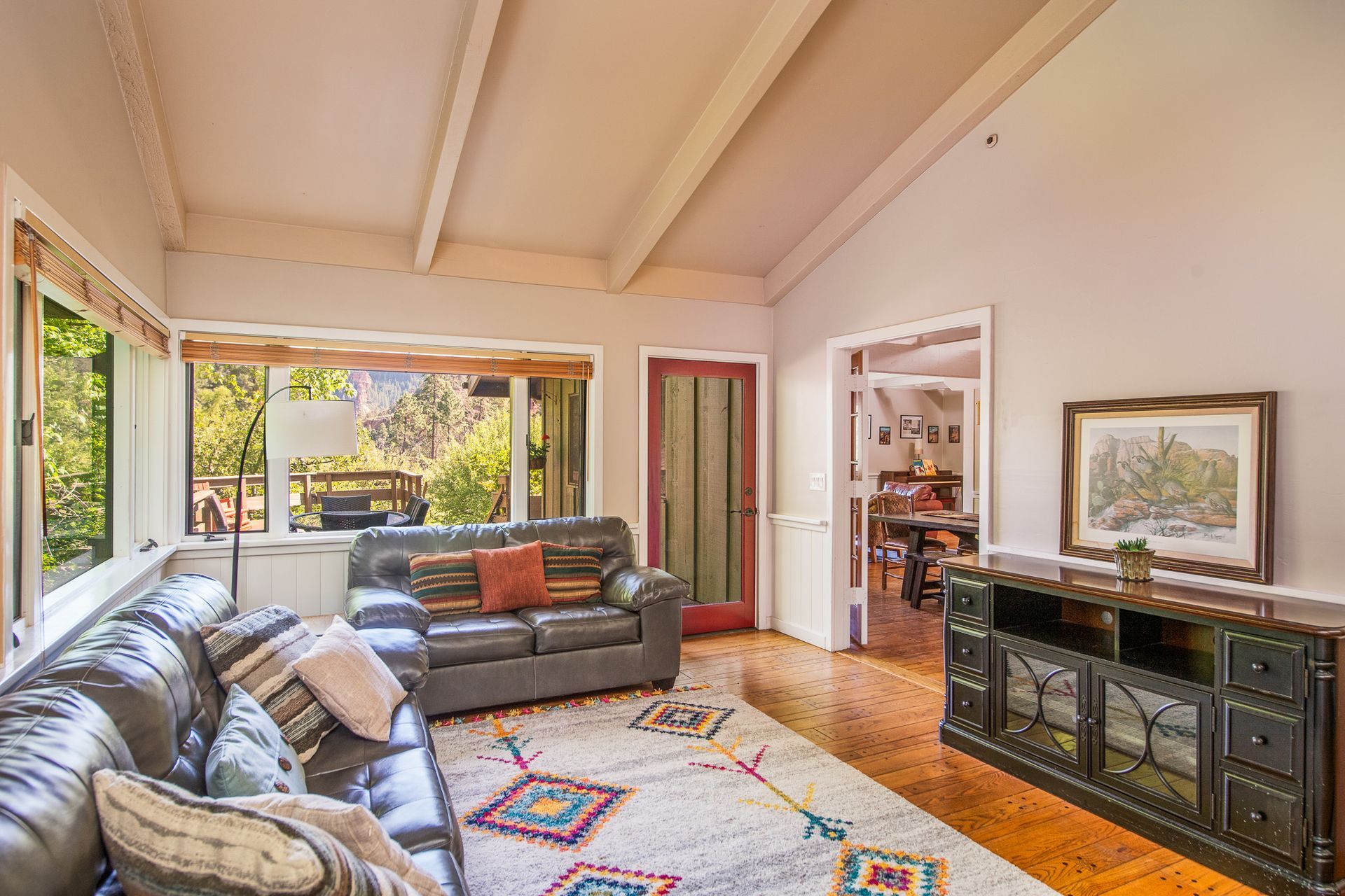 Bright living room with a sofa, colorful rug, open doors to a garden, and a dark cabinet with decor.