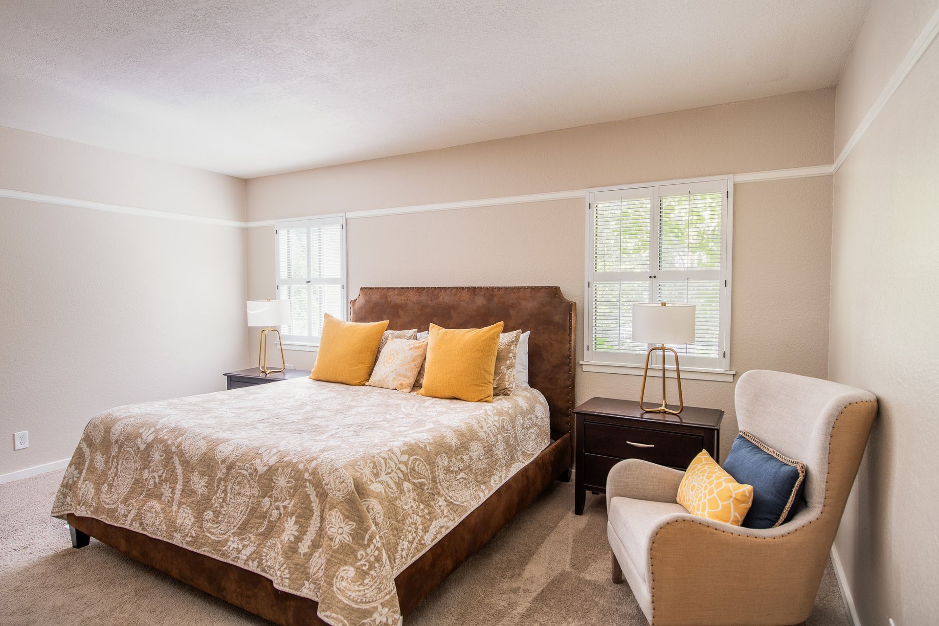 Bright bedroom with a large bed, yellow pillows, two windows, and a chair by the window.