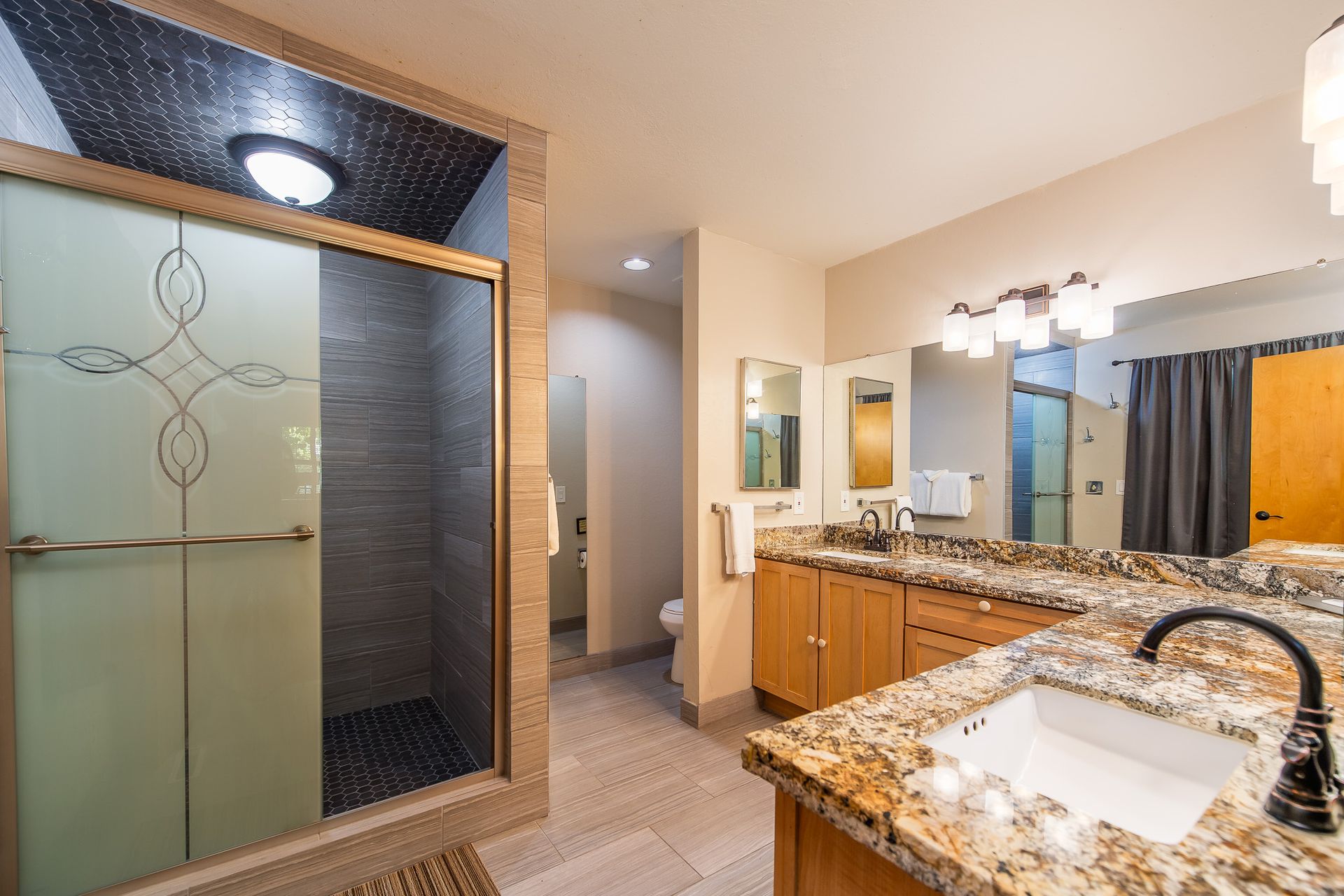Modern bathroom with glass shower, granite vanity, large mirror, and tiled walls