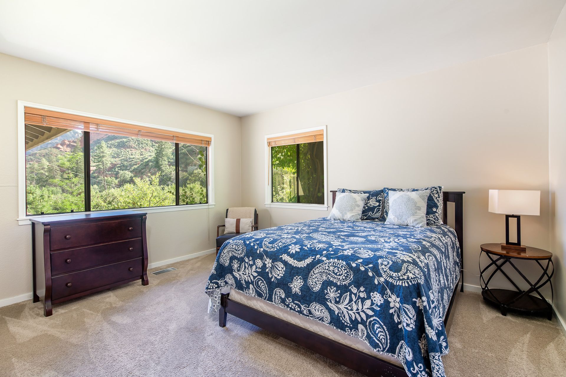 Bright bedroom with blue floral bedspread, dresser, window, and bedside lamp