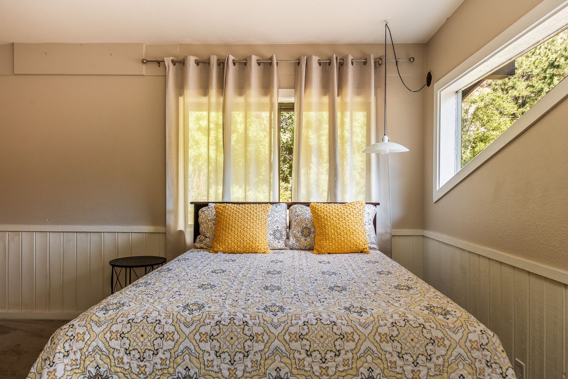 Bright bedroom with a bed, floral duvet, yellow pillows, and curtains by a window