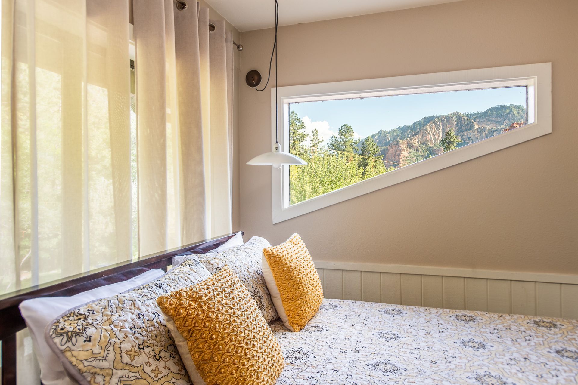 Bright bedroom with a bed, patterned pillows, and a slanted window showing trees outside
