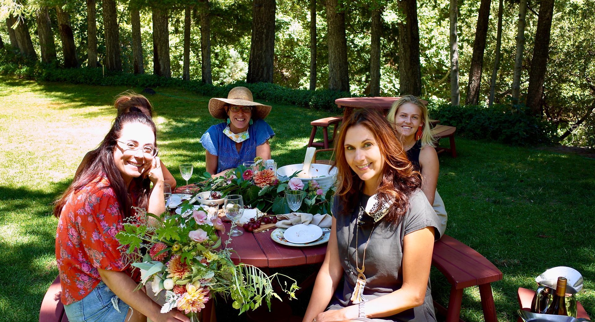 People gathered around a picnic table in a sunny garden, with flowers and drinks outdoors.