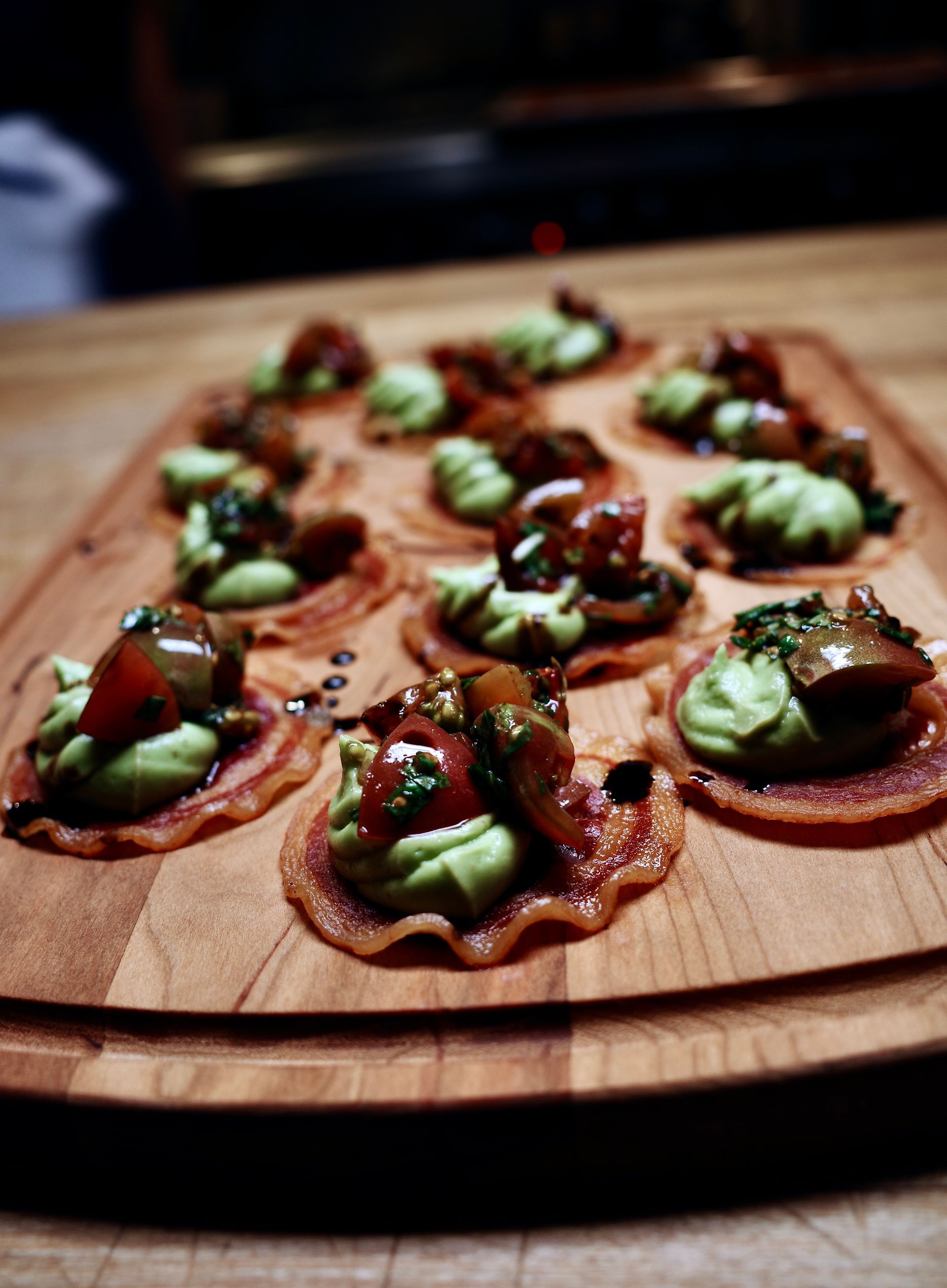 Plated avocado and strawberry toast bites on a wooden board, topped with herbs and dark sauce