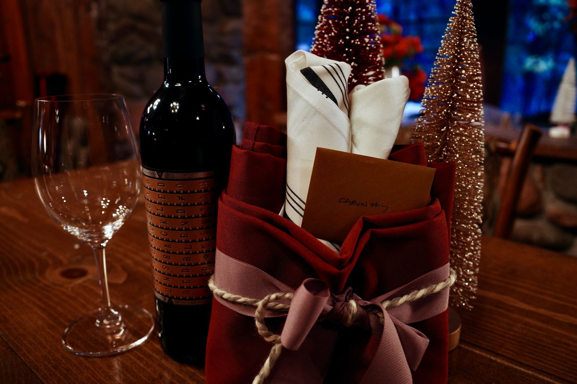 Holiday table setting with wine bottle, glass, and festive gift basket with ribbons and decorations