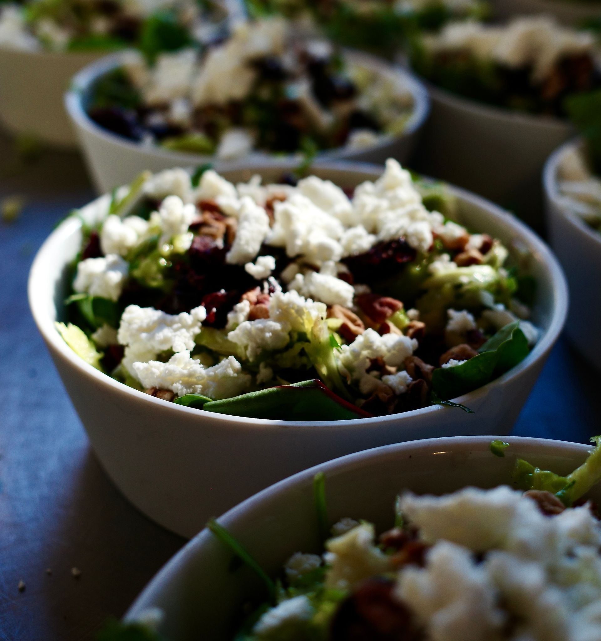 Bowls of leafy salad topped with crumbled cheese on a table, softly lit.