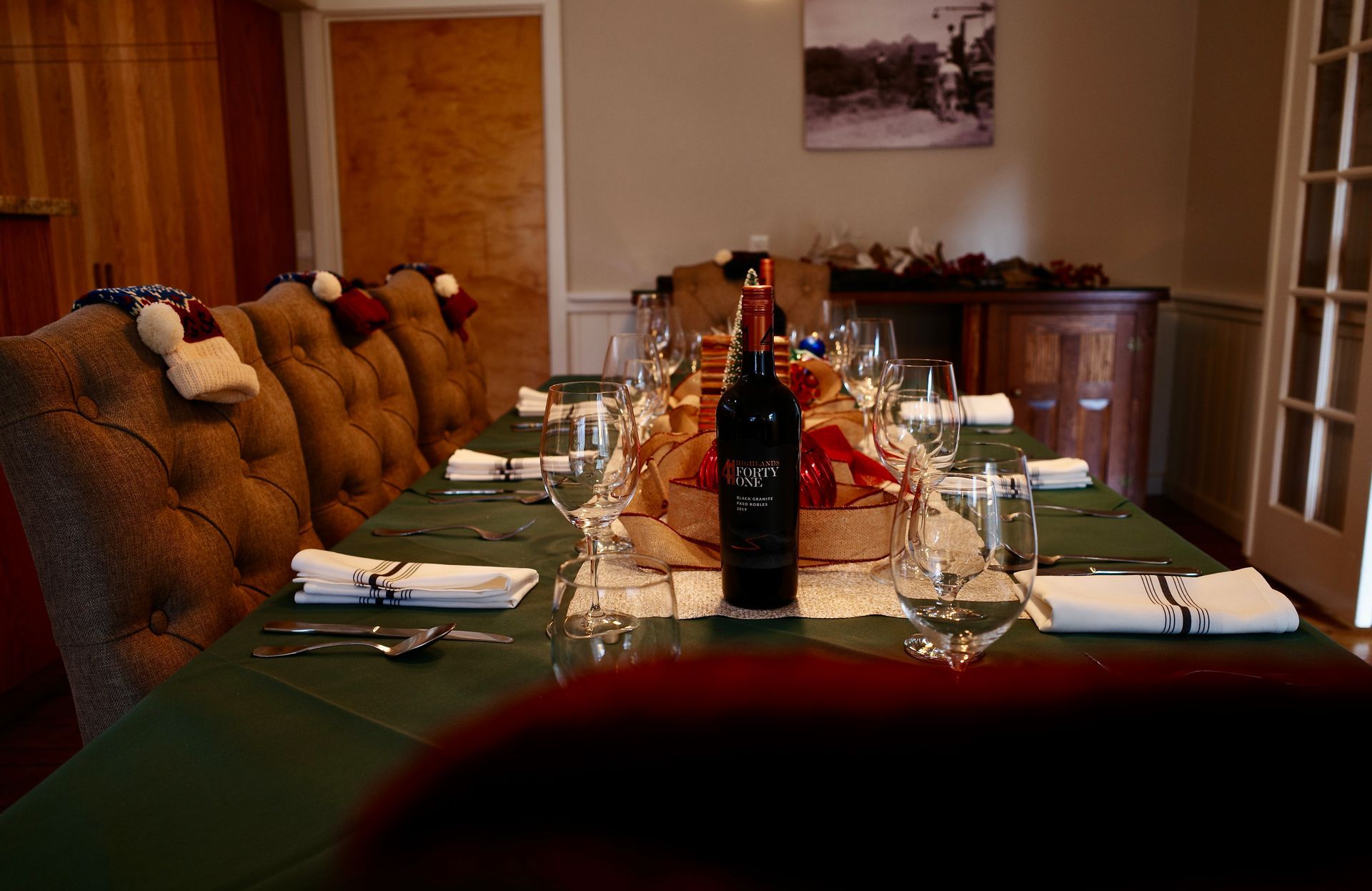 Long dining table set with green runners, wine bottles, glassware, and cushioned bench seating in a cozy room