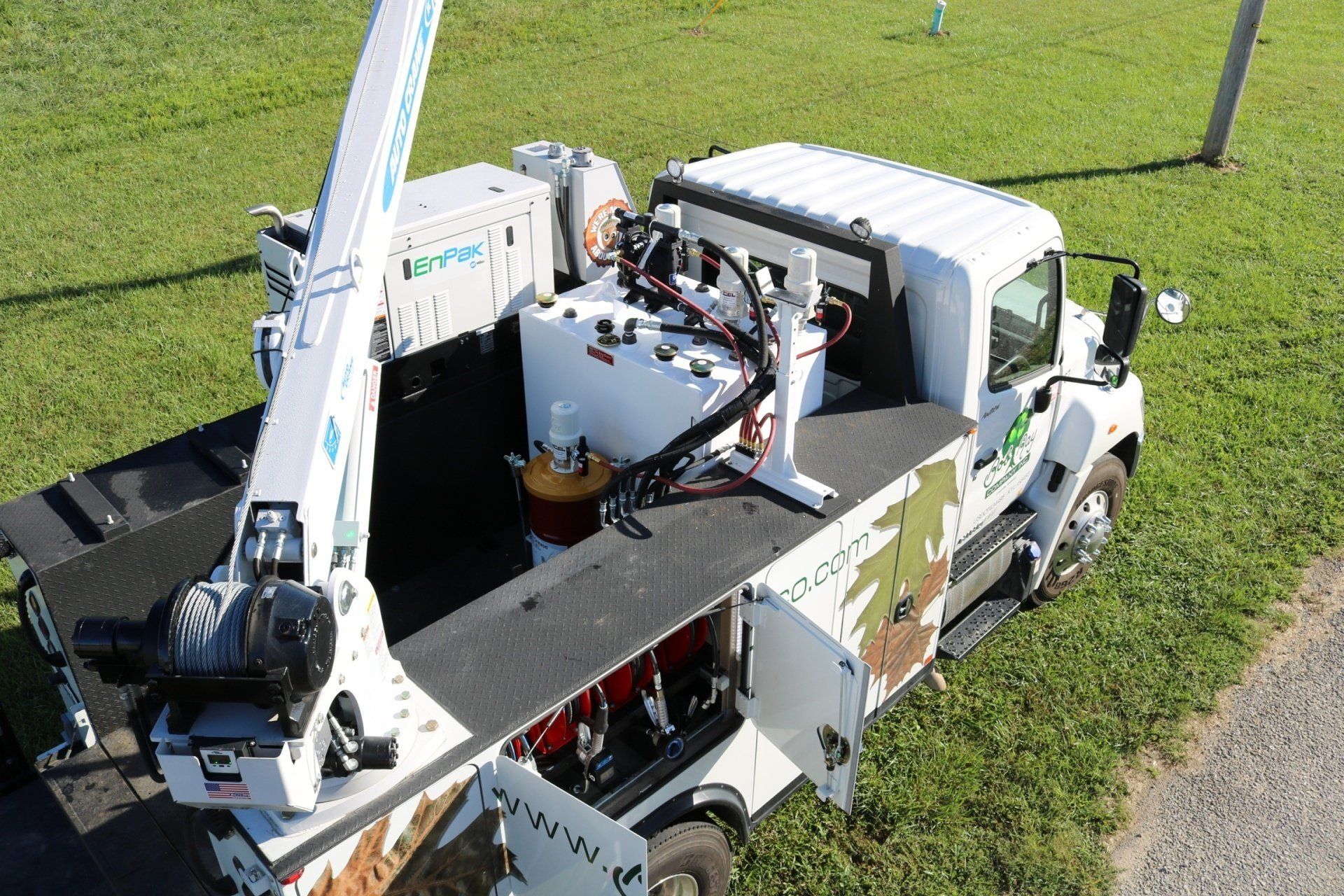 An overhead view of a white utility truck with a crane attachment, parked on grass next to a gravel area.