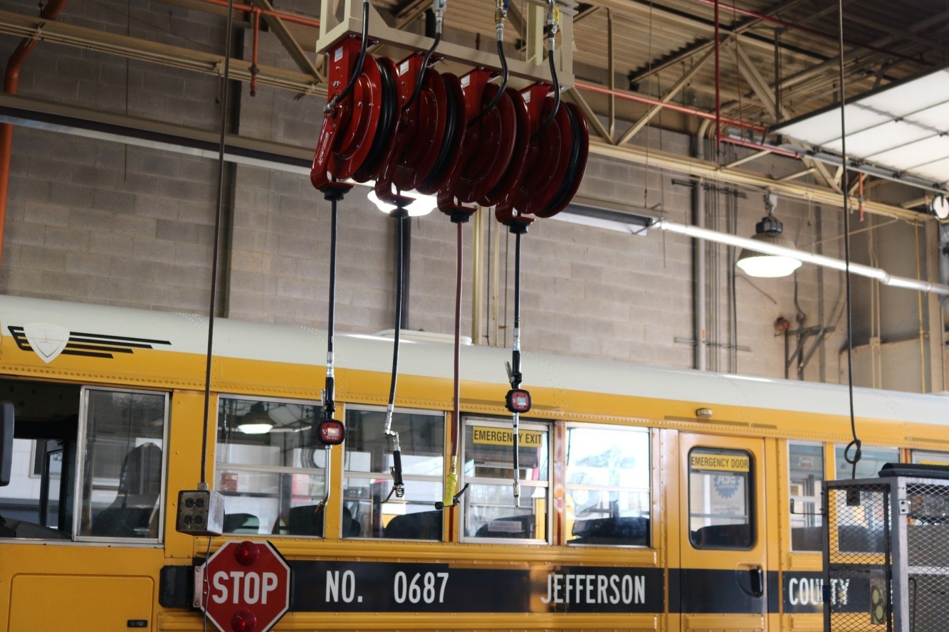 Red hanging hose reels suspended above a yellow school bus parked inside a maintenance garage.