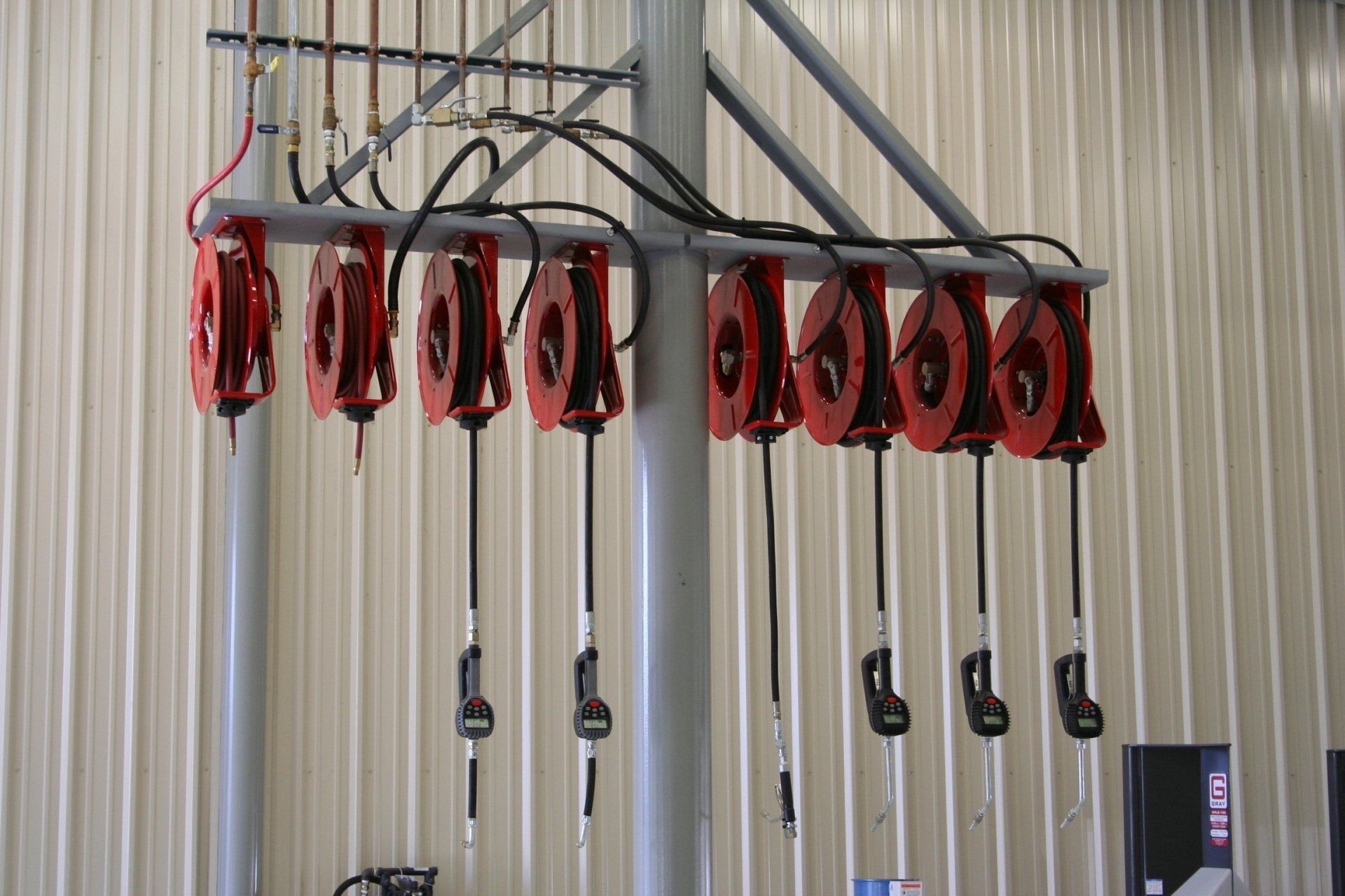 A row of red industrial hose reels with dispensing nozzles suspended from a ceiling-mounted rack in a workshop.
