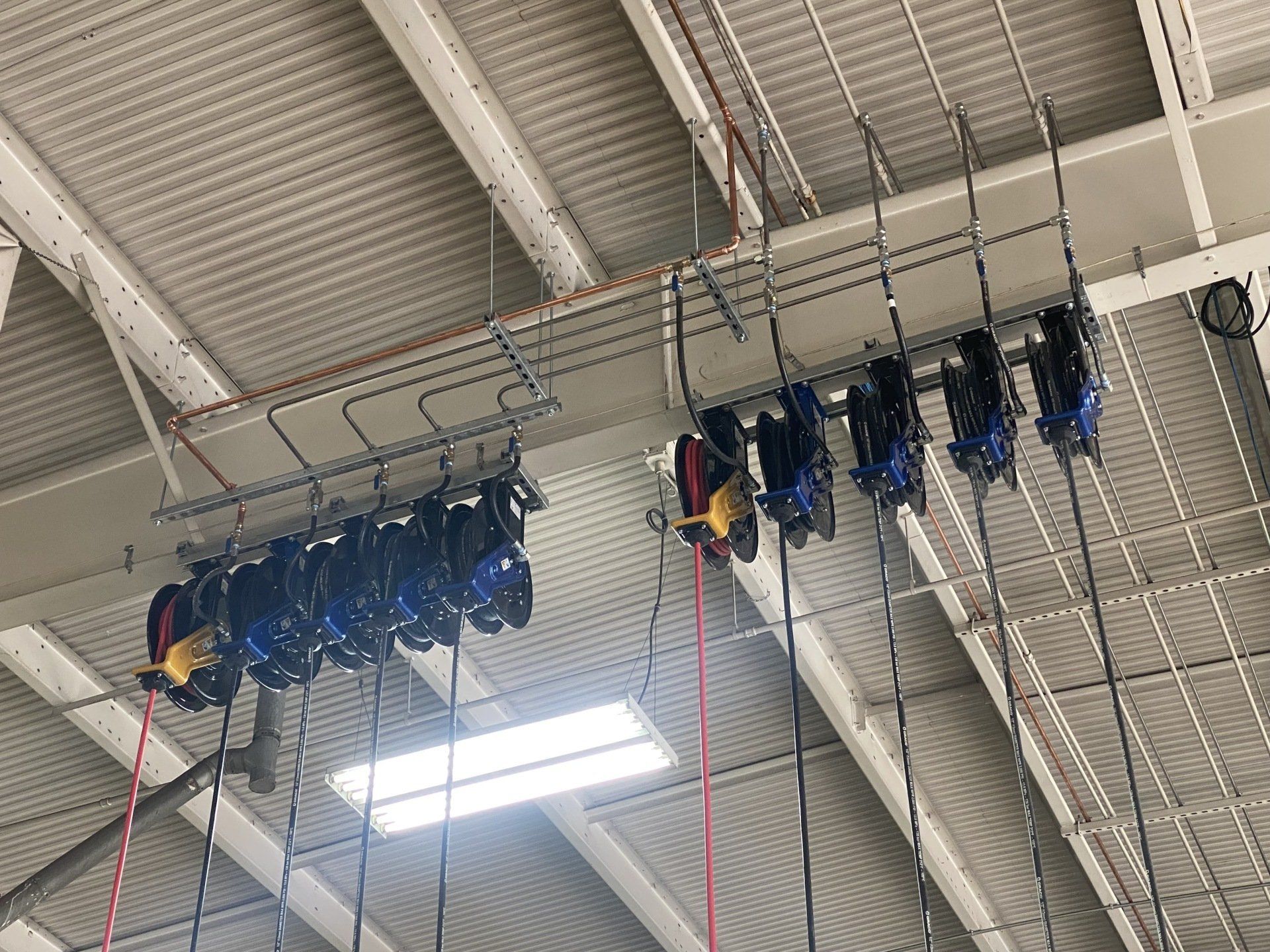 Rows of blue and black ice skates hanging from racks attached to a metal ceiling in an indoor sports facility.
